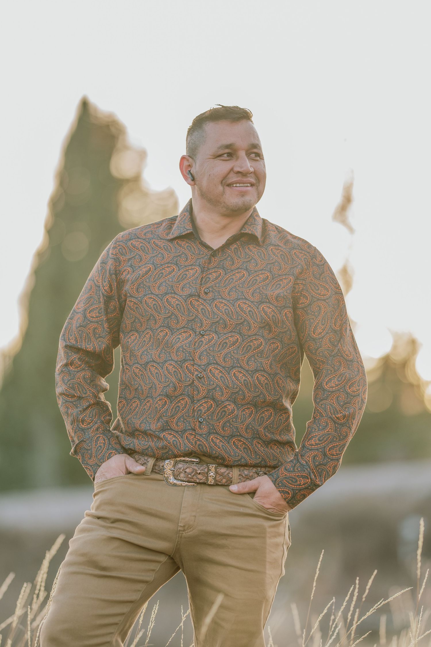 Outdoor portrait of someone wearing a brown patterned sweater and khaki pants standing in golden evening light.
