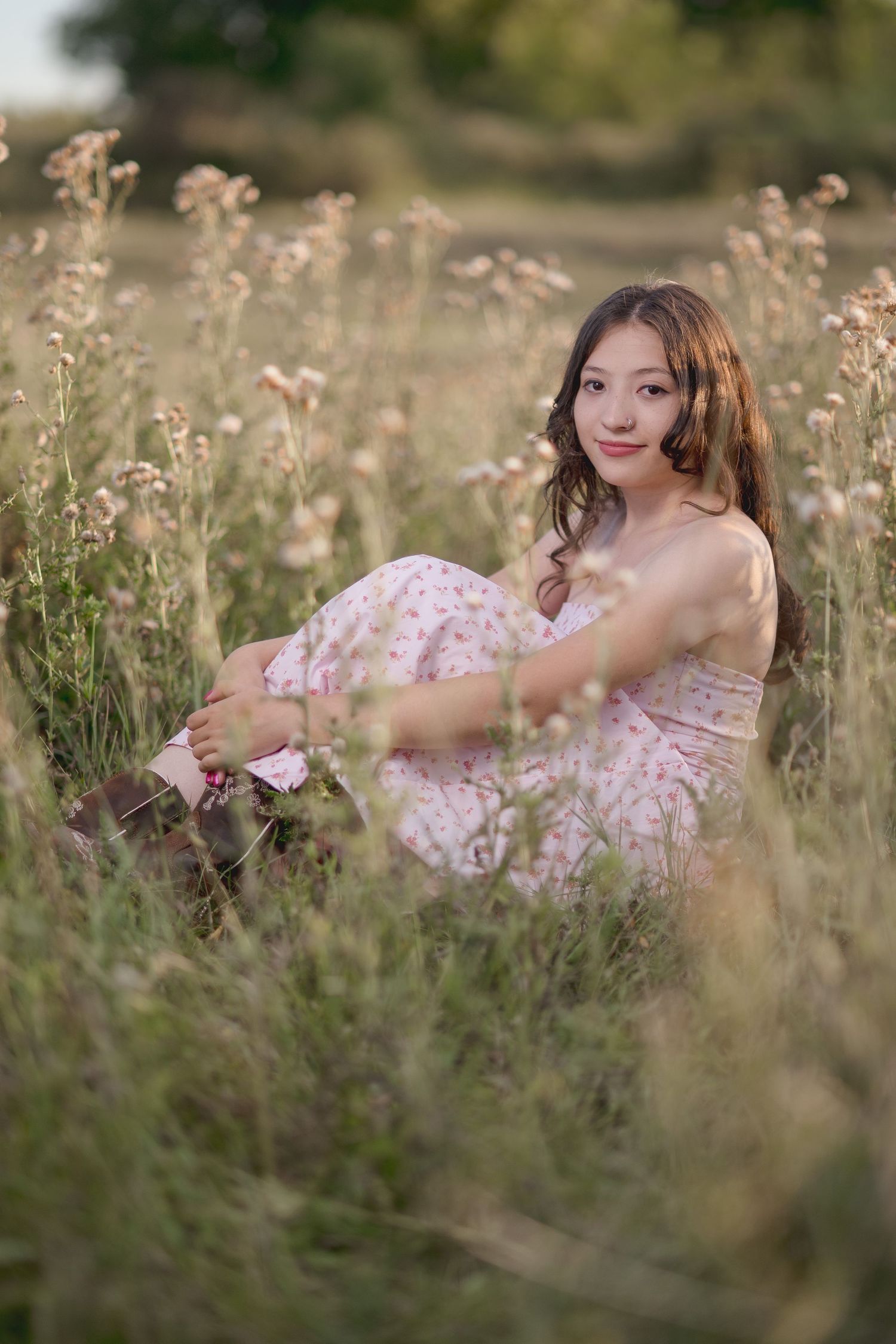 A person in a pink floral dress relaxes in a wildflower meadow during a dreamy summer photoshoot.