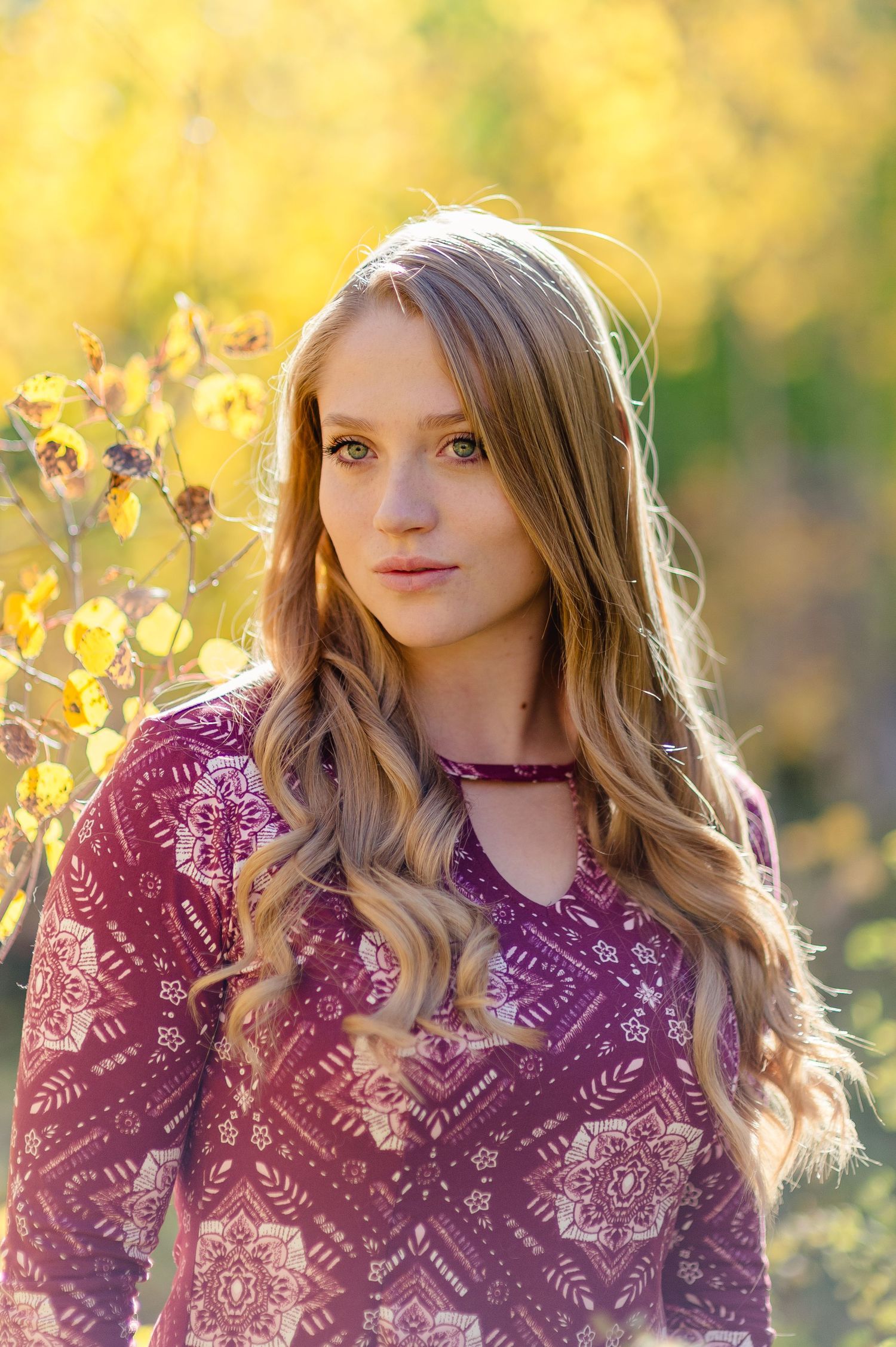 Stylish burgundy lace dress with wavy blonde hair captured in warm autumn sunlight against yellow foliage background.