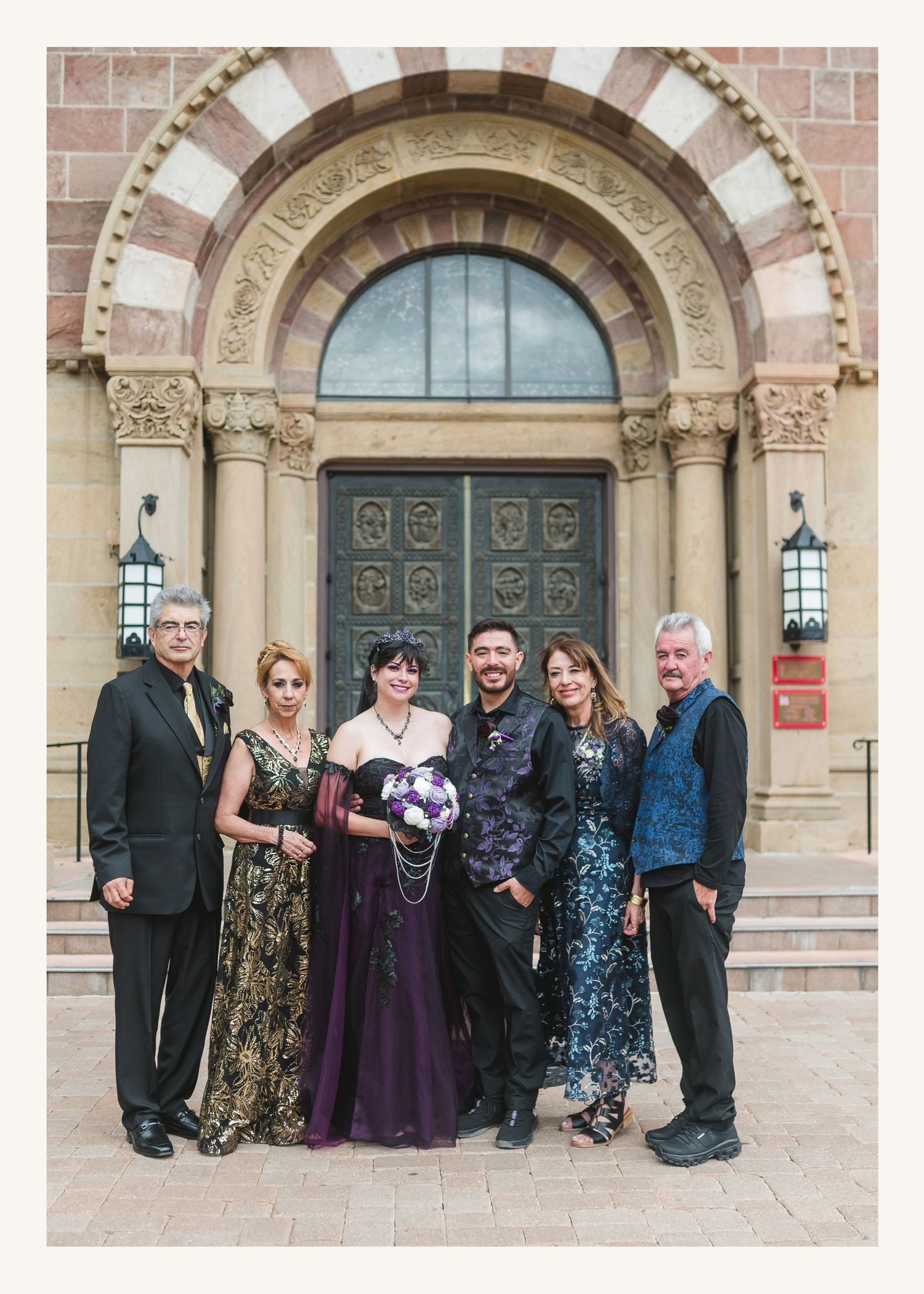 Six elegantly dressed people posing together in front of ornate church doors at a wedding celebration.