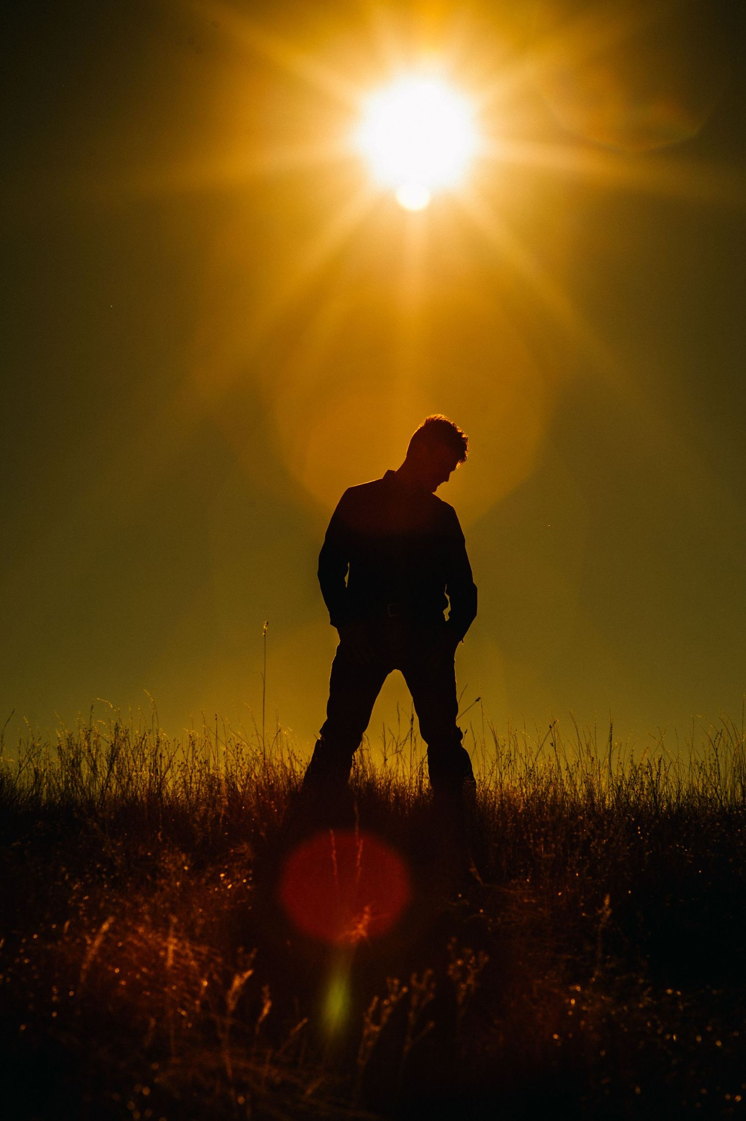 Silhouette of a man standing in a field at golden sunset with dramatic sun rays and lens flare.