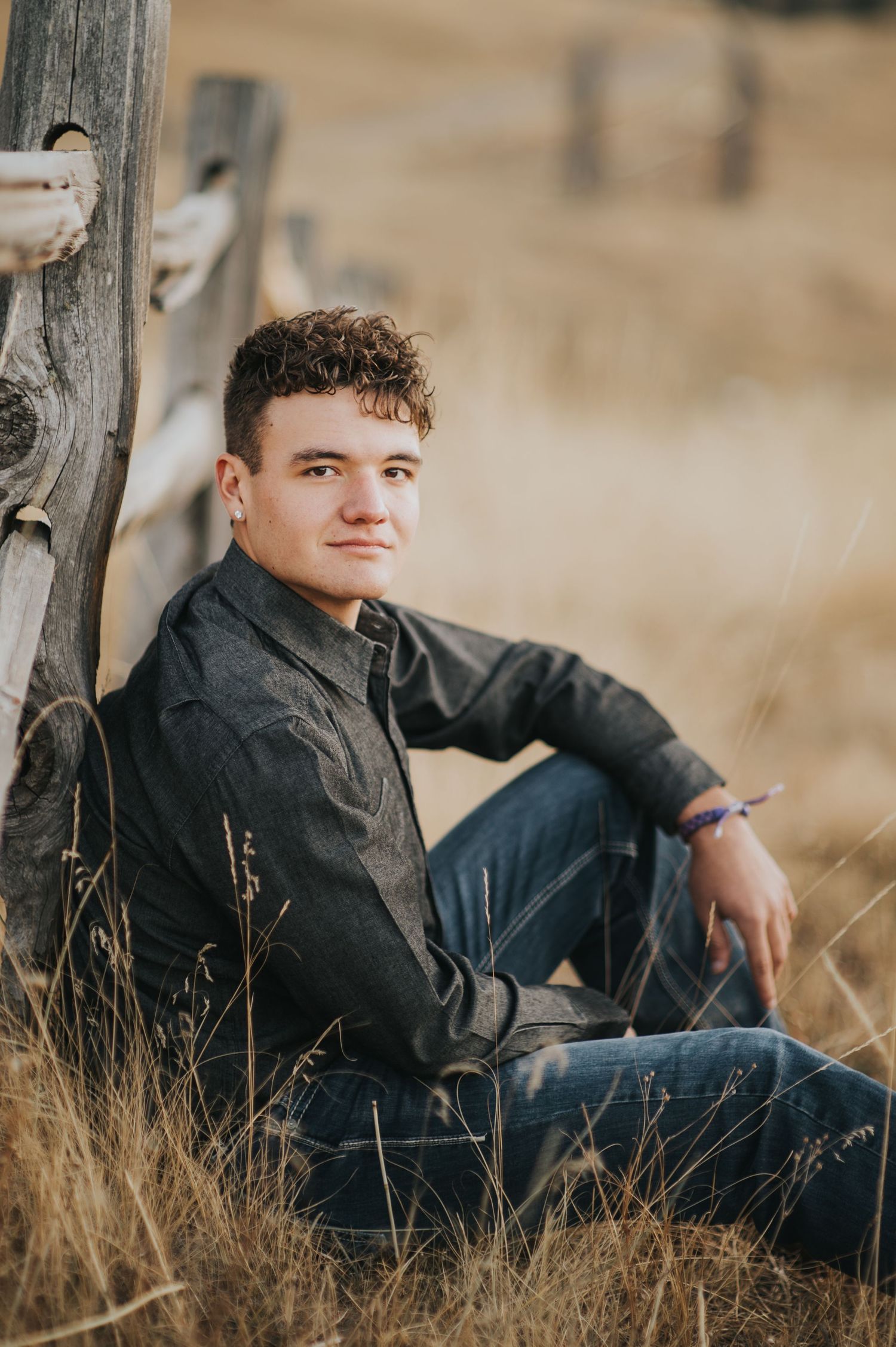 Casual outdoor portrait leaning against wooden fence post in field.