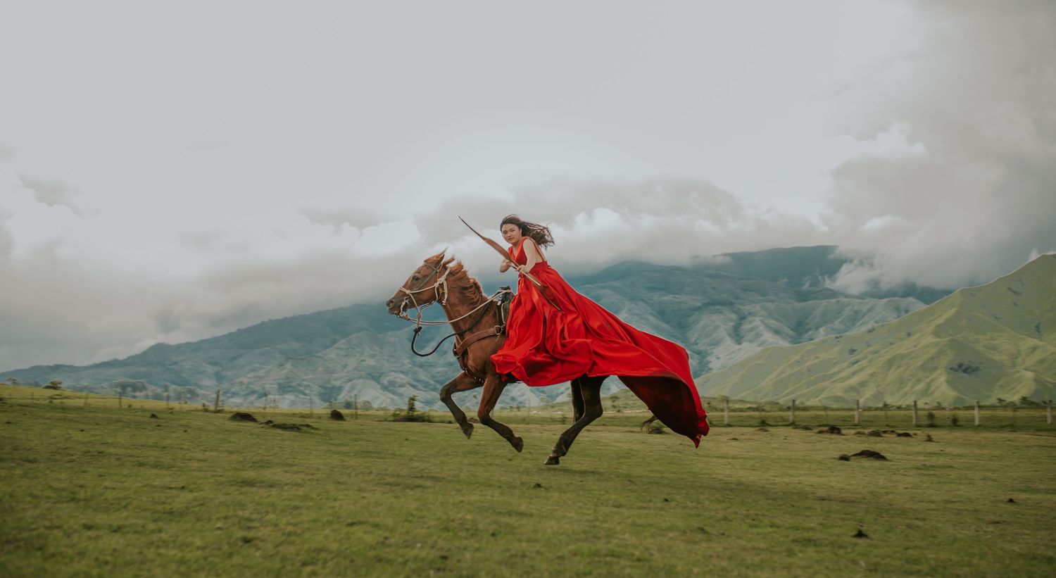 Horse galloping across mountainous terrain with flowing red fabric in motion.