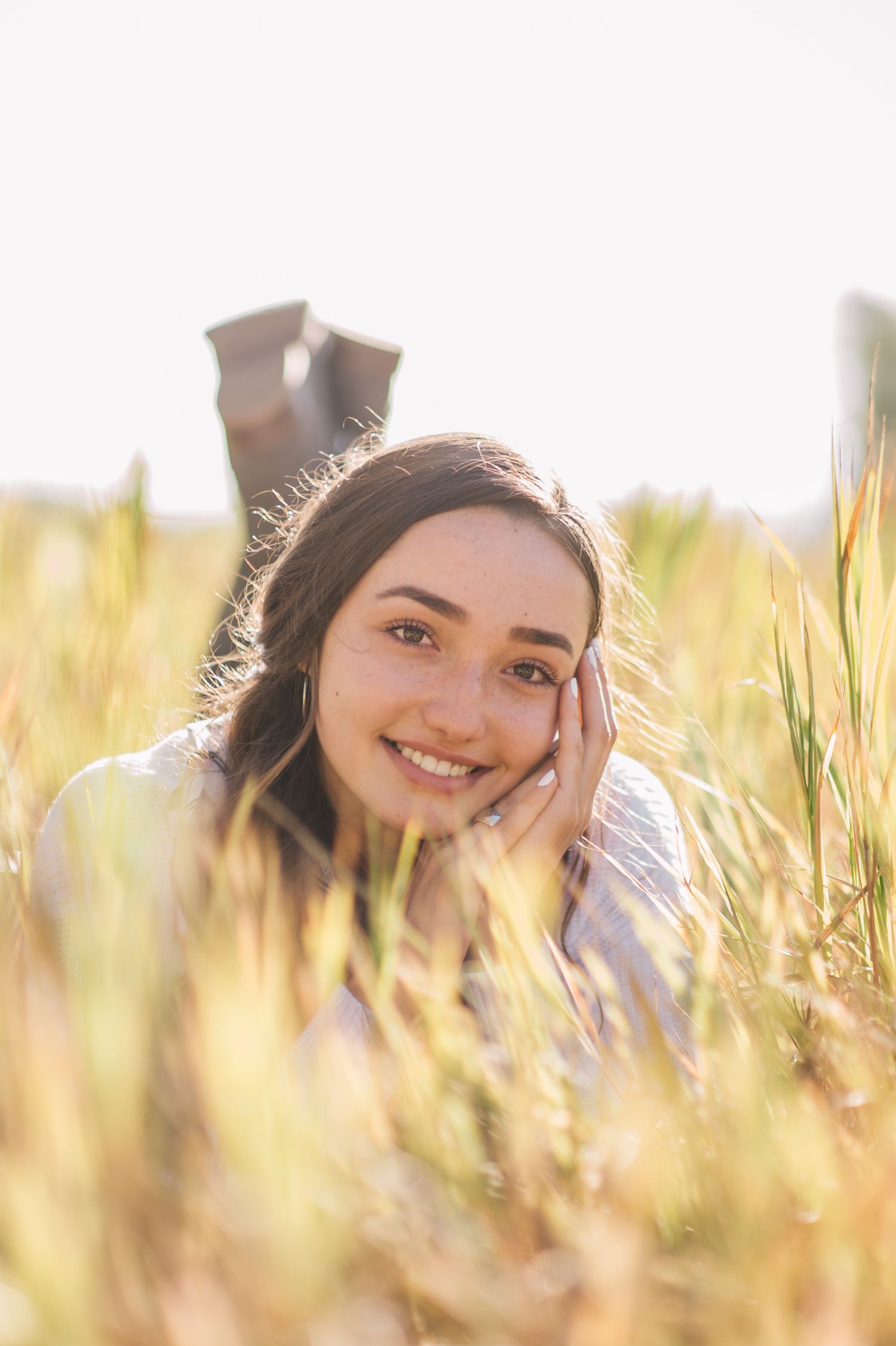 Senior girl sitting in a green field, with gentle sunlight highlighting her features, by Quiet Light by The Amoras.