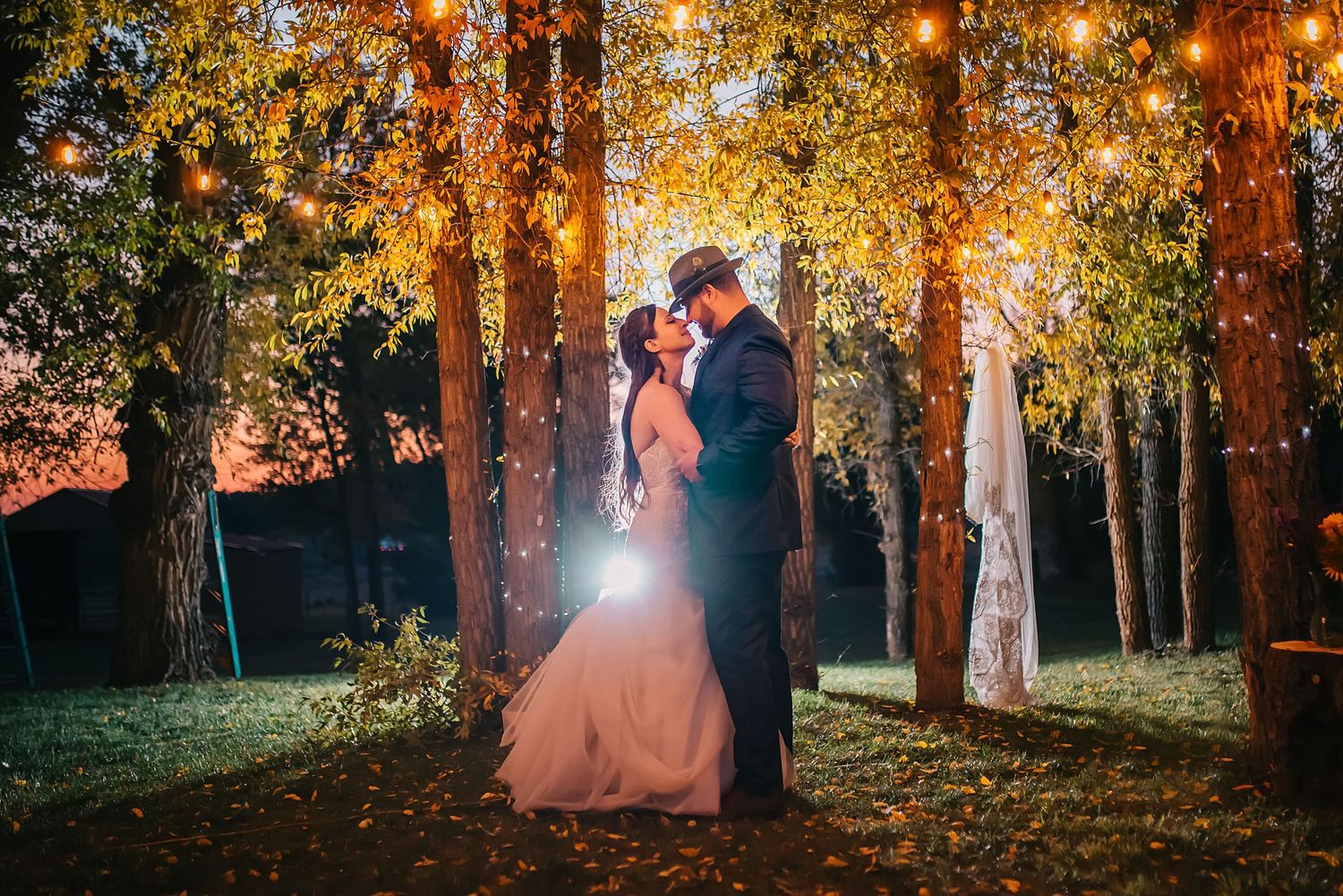 Newlyweds share a romantic moment under glowing autumn trees at dusk.