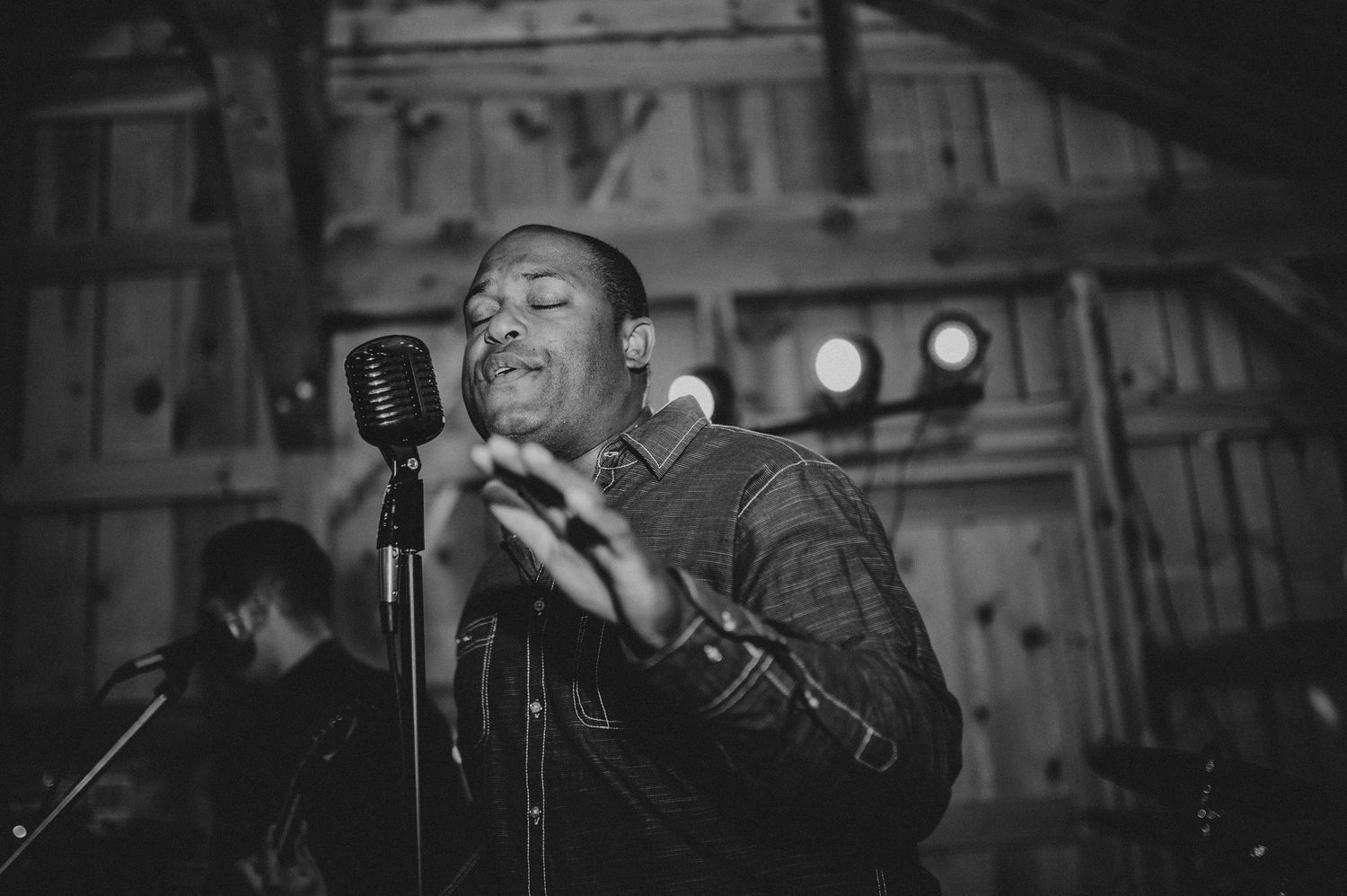 Black and white image of a performer singing passionately into a vintage microphone on stage.