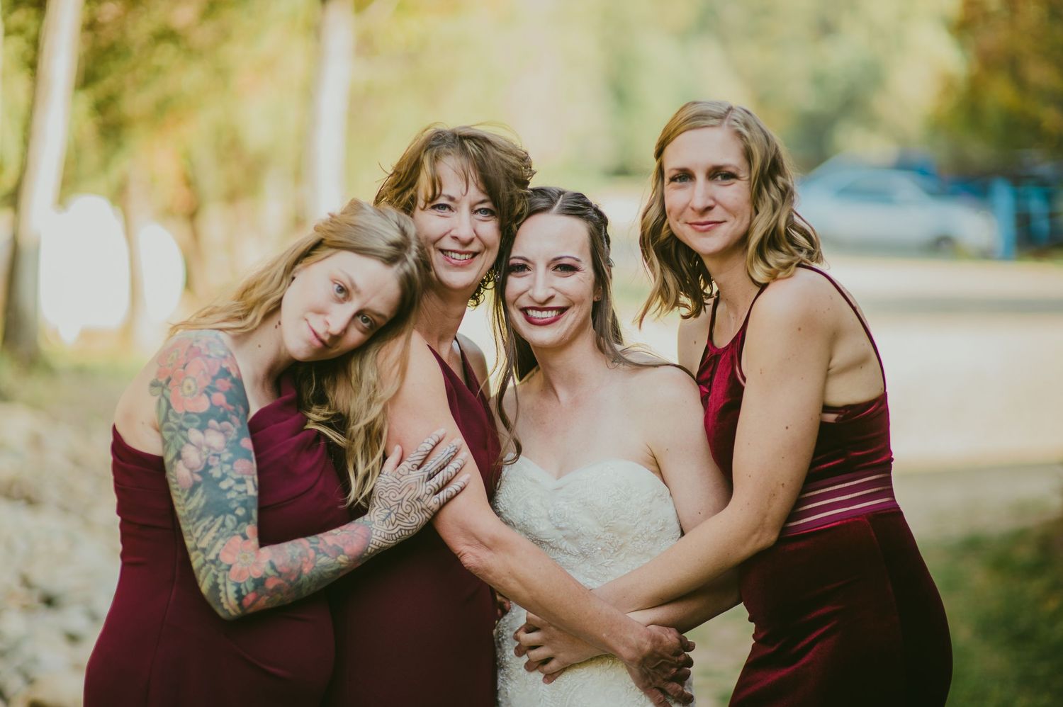 Wedding party wearing burgundy dresses pose together outdoors in fall setting.
