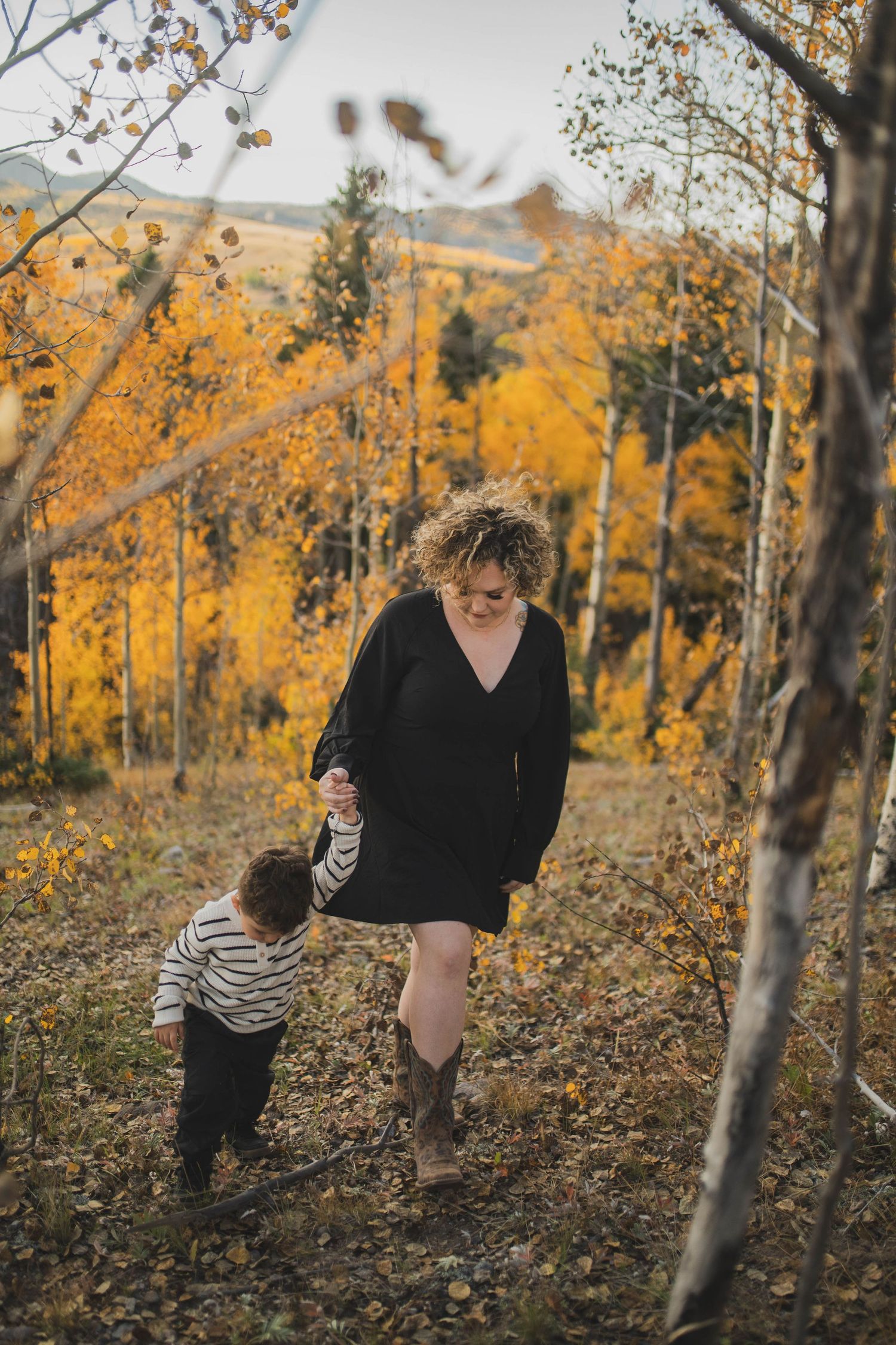 Fall photo of mom and child walking in forest with golden leaves — natural and heartfelt image by The Amoras in New Mexico.