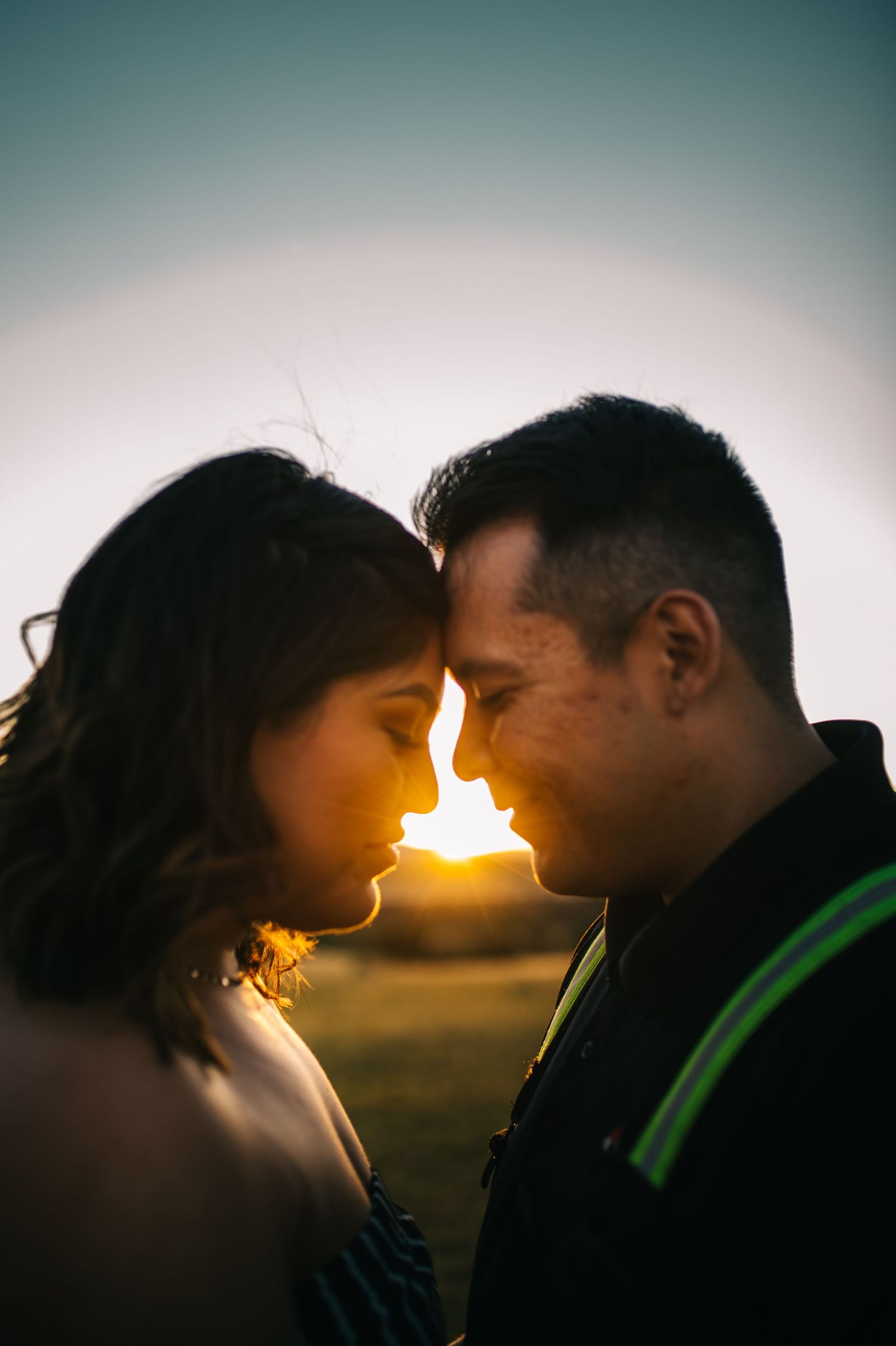 Backlit silhouettes of a couple nuzzling noses during sunset.