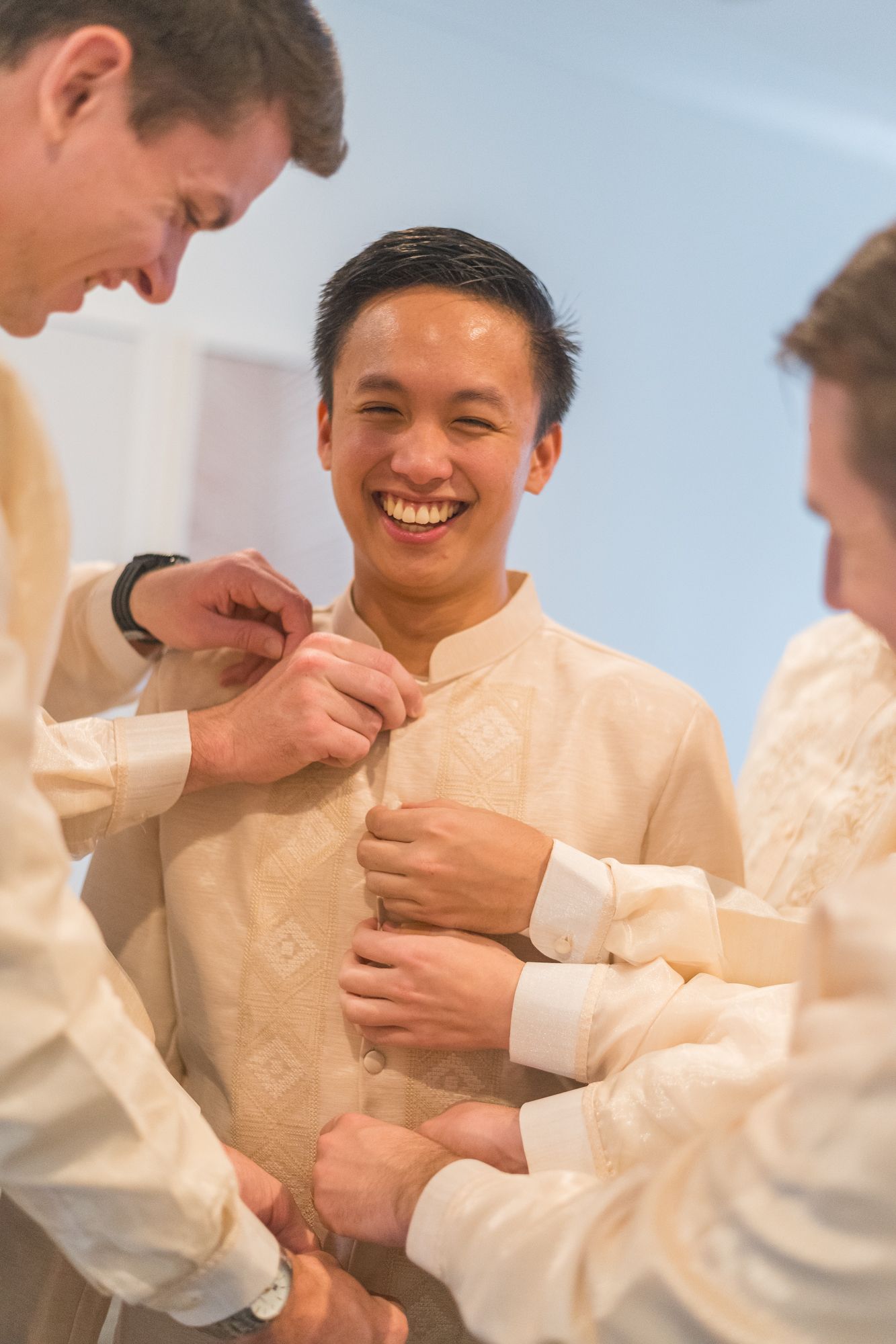 People in cream-colored traditional barong tagalog shirts share joyful laughter during a celebration.