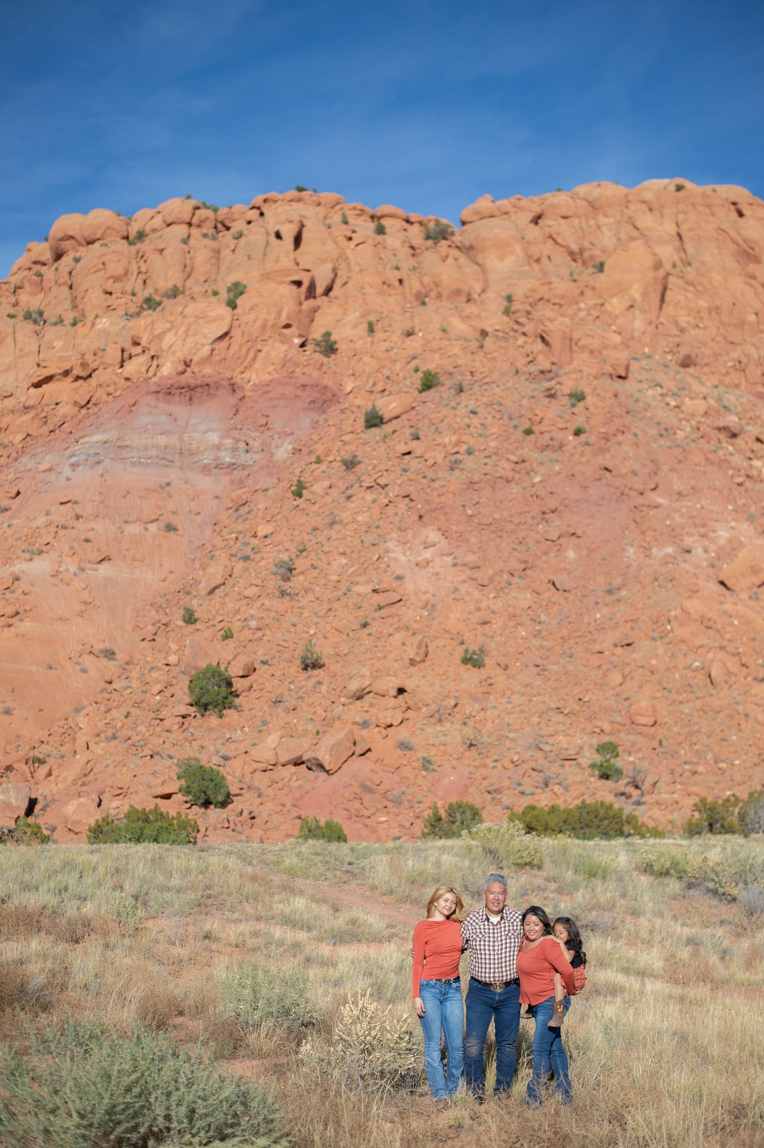 Three people stand in front of a towering red sandstone cliff formation at Garden of the Gods park in Colorado.