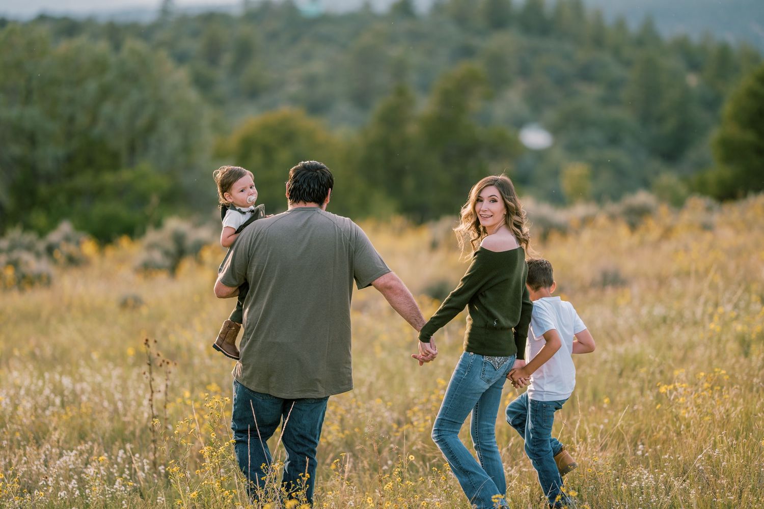 Family holding hands while walking through field of yellow wildflowers.