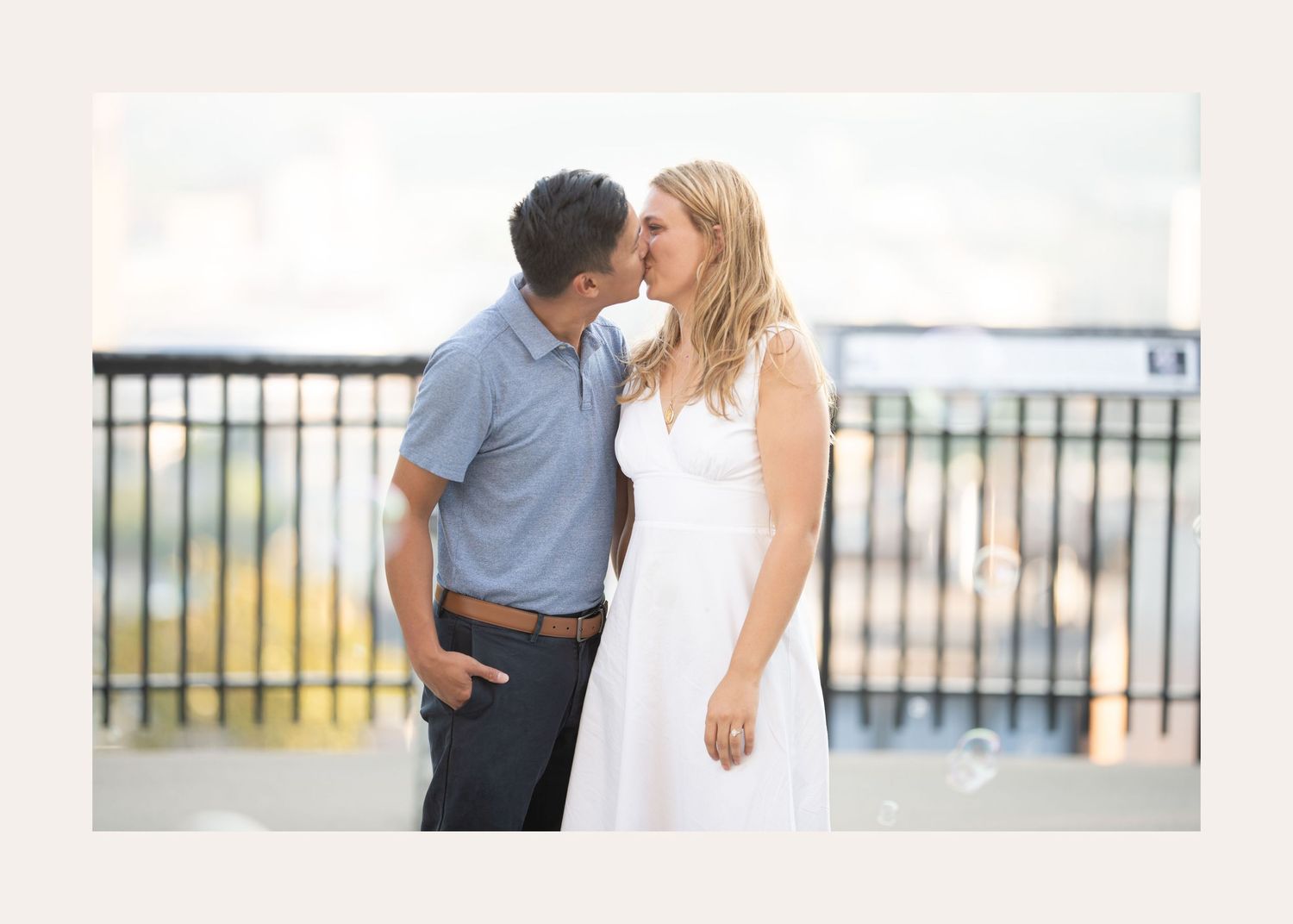 A couple shares a romantic moment on an outdoor balcony overlooking a city, with the individual in white and blue attire.