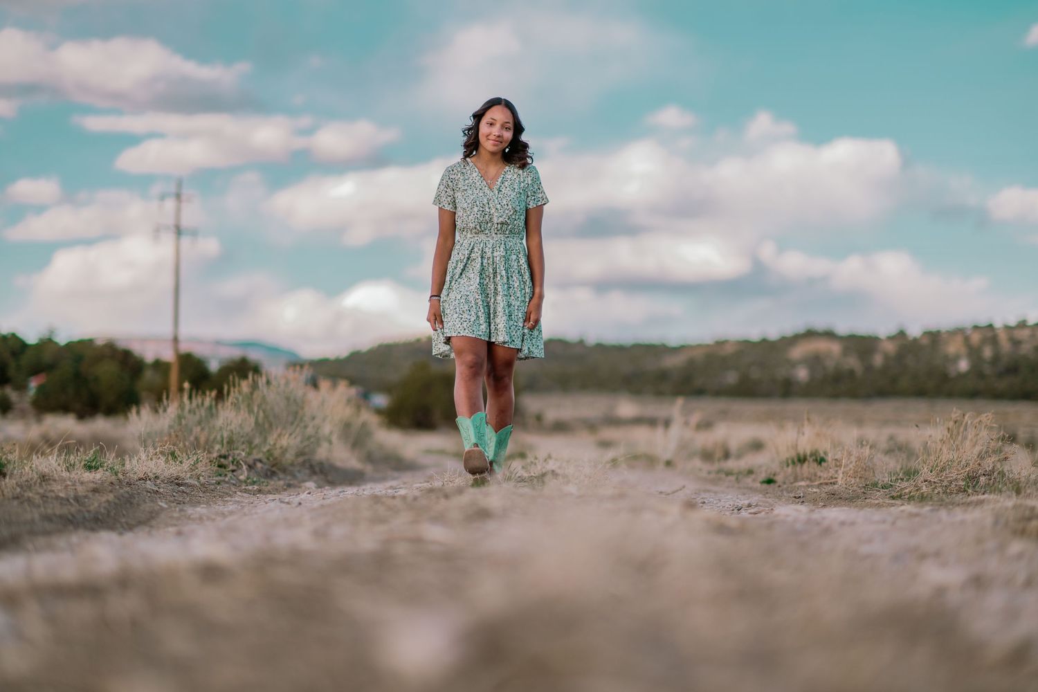 A figure in a turquoise dress stands confidently against a desert landscape at sunset.