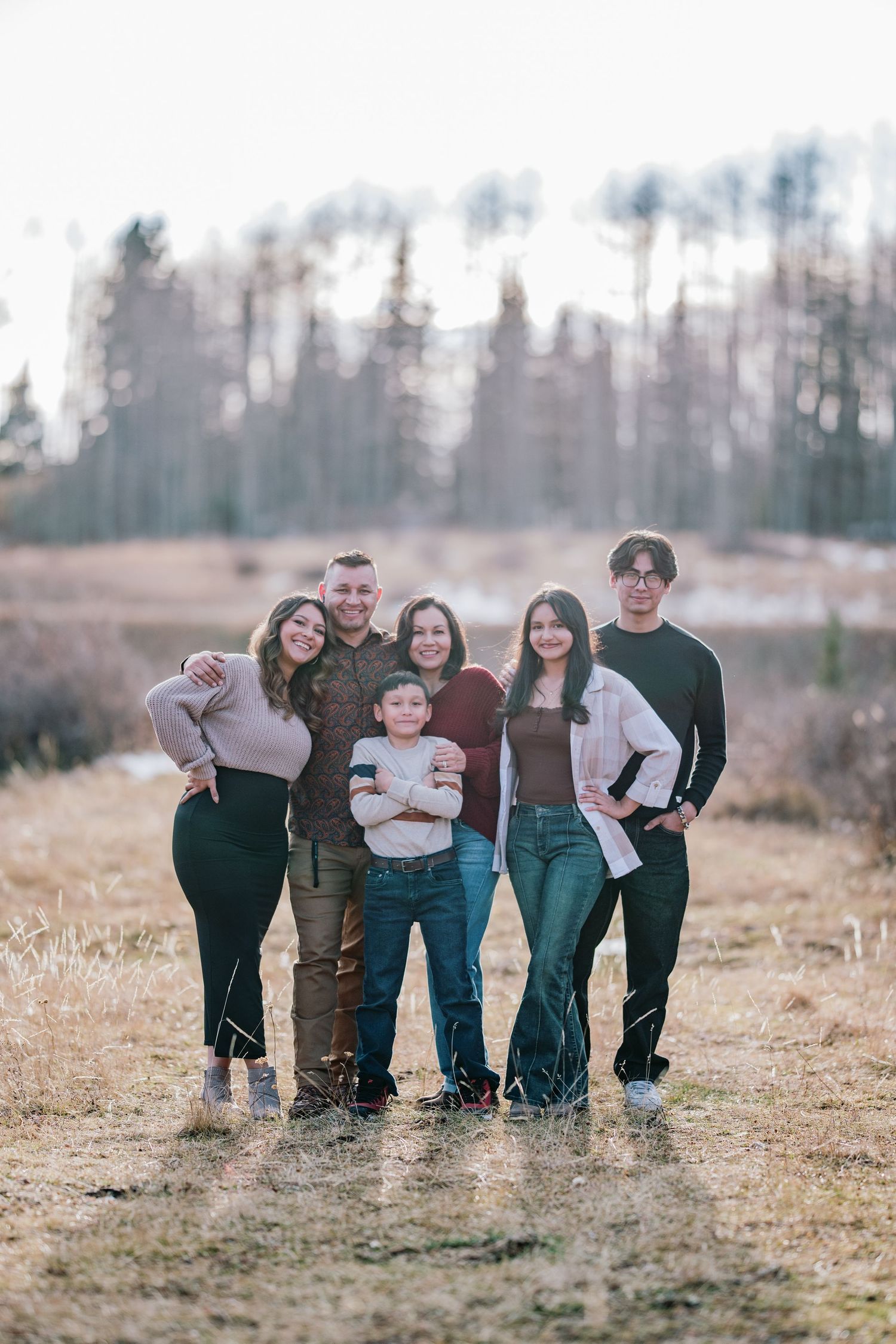 A group stands together outdoors in casual clothing against a backdrop of winter trees in soft natural lighting.