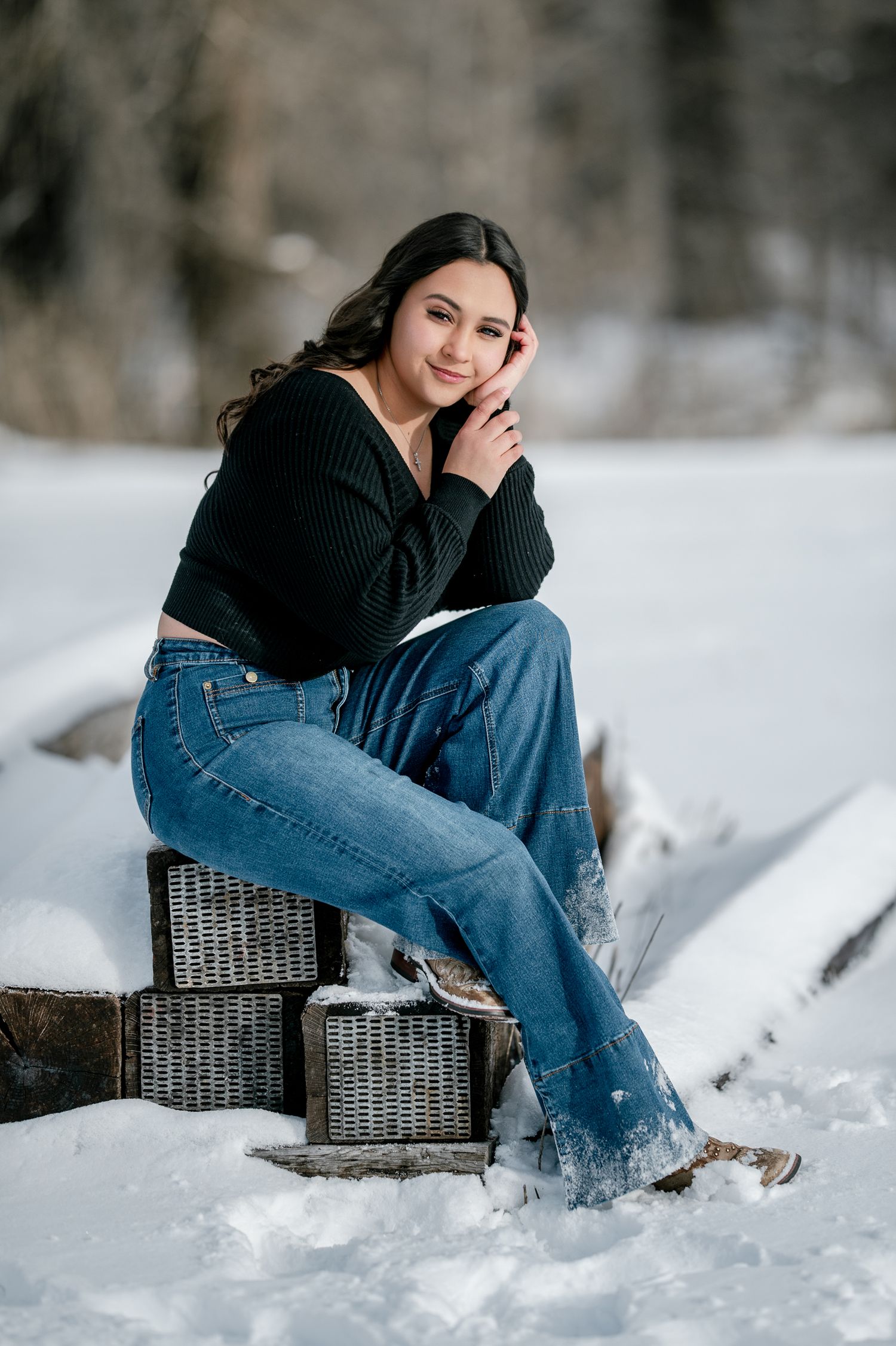 A person in a black sweater and blue jeans sits on a wicker chair in a snowy winter setting.