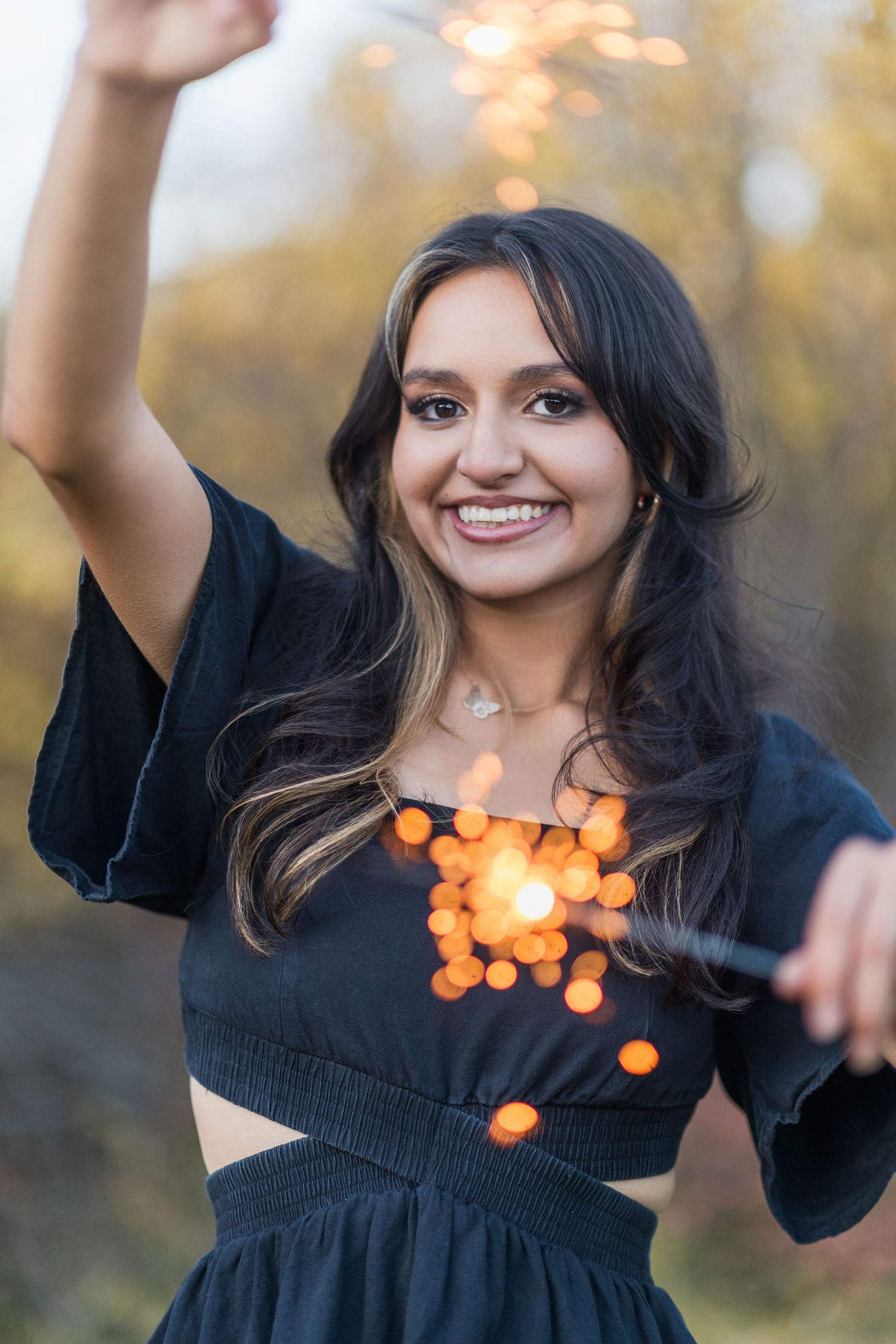 A woman in a black dress dances joyfully outdoors with bokeh lights creating a magical autumn atmosphere.