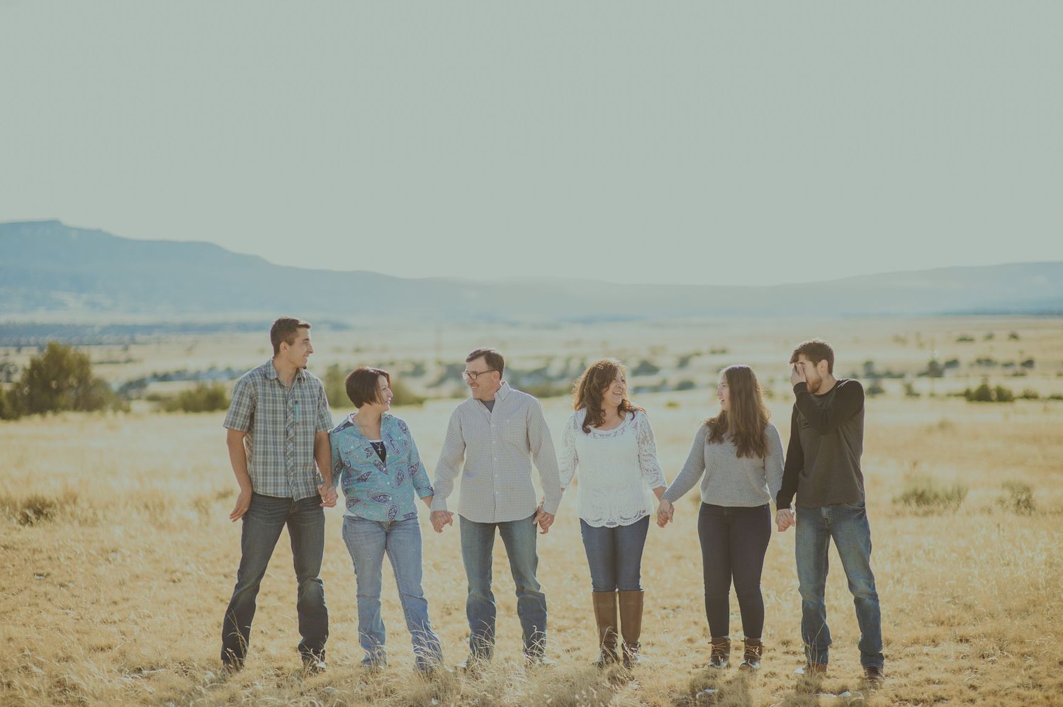 Family of six walking hand-in-hand through the golden sands of Abiquiú's desert — natural light portrait by The Amoras.