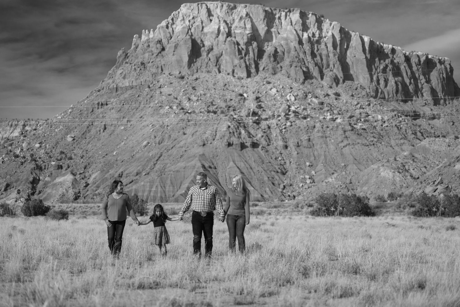 A silhouetted family group walks together in a desert landscape with dramatic red rock formations rising in the background.