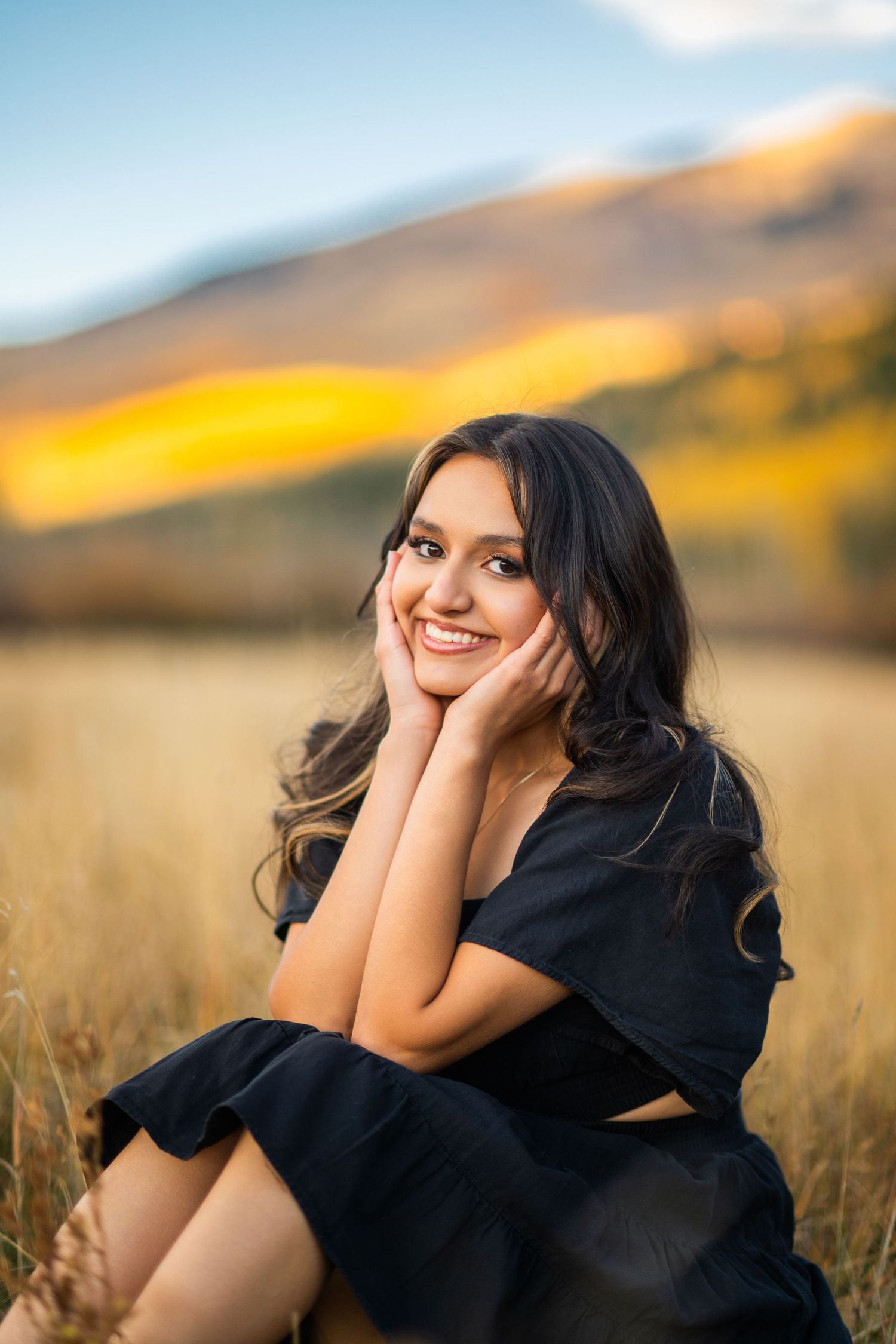 A person in a black top poses expressively in a golden wheat field at sunset.