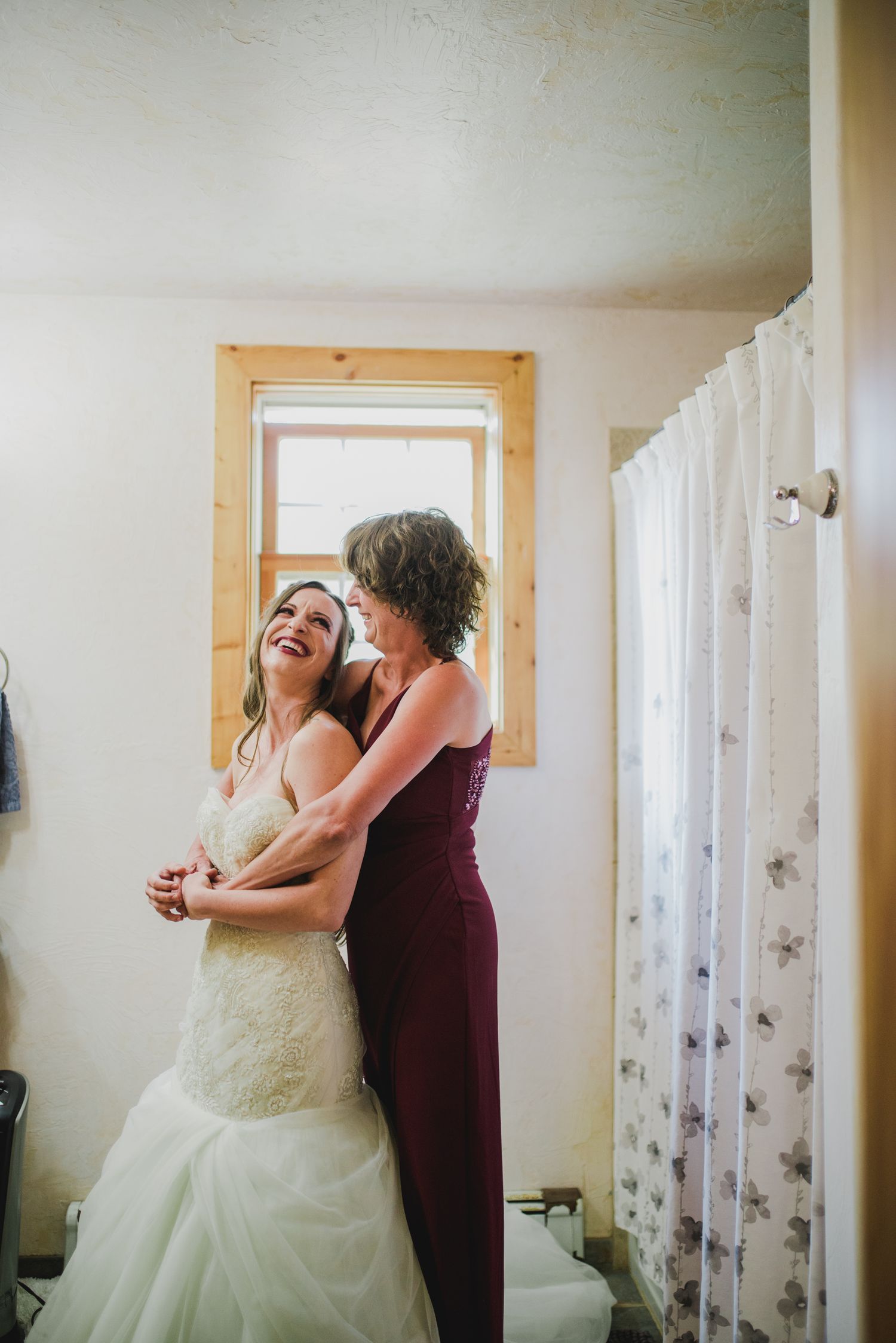 Emotional getting ready moment captured in bright indoor setting with white curtains.