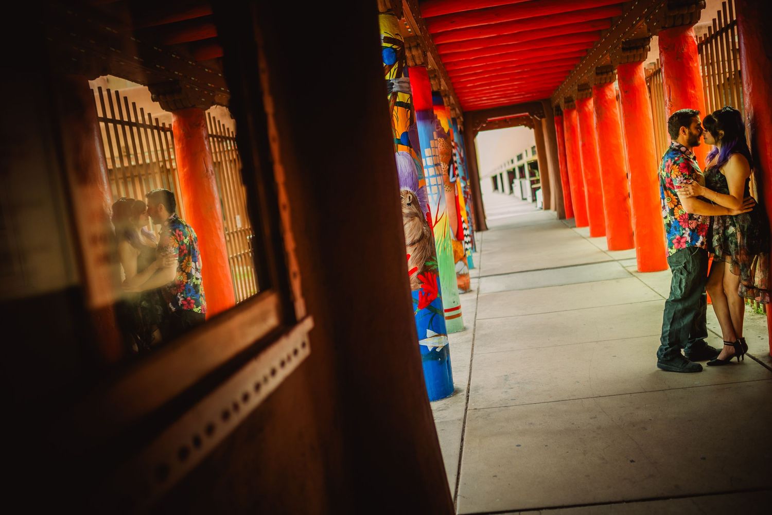 Couple embracing in a vibrant red columned corridor with colorful murals at a cultural temple venue.