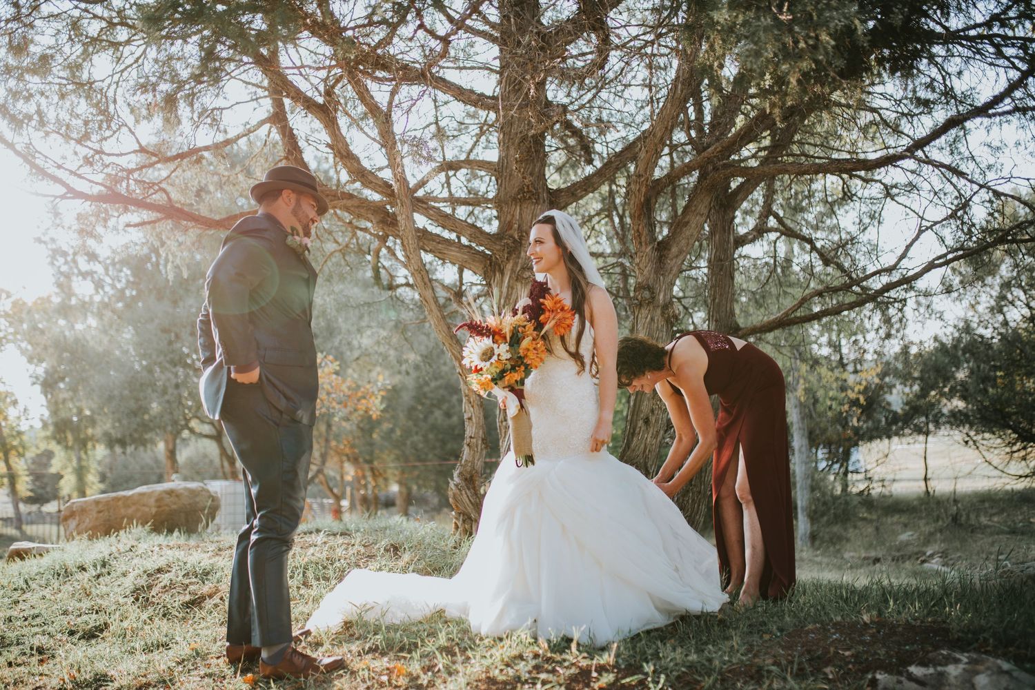 Couple getting married outdoors under a canopy of trees during a sunlit autumn ceremony.