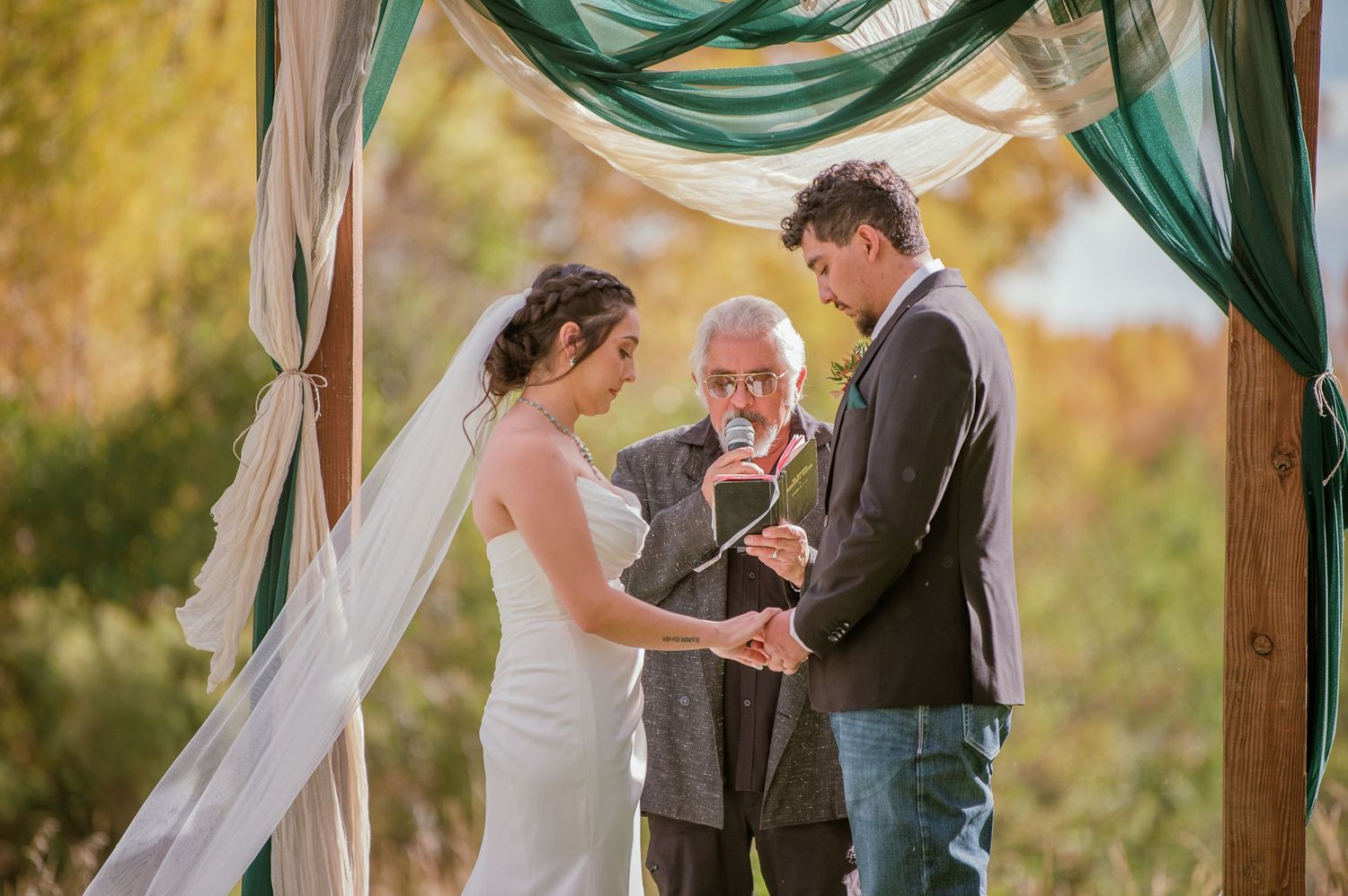 Intimate outdoor wedding ceremony under draped arch with teal accents.