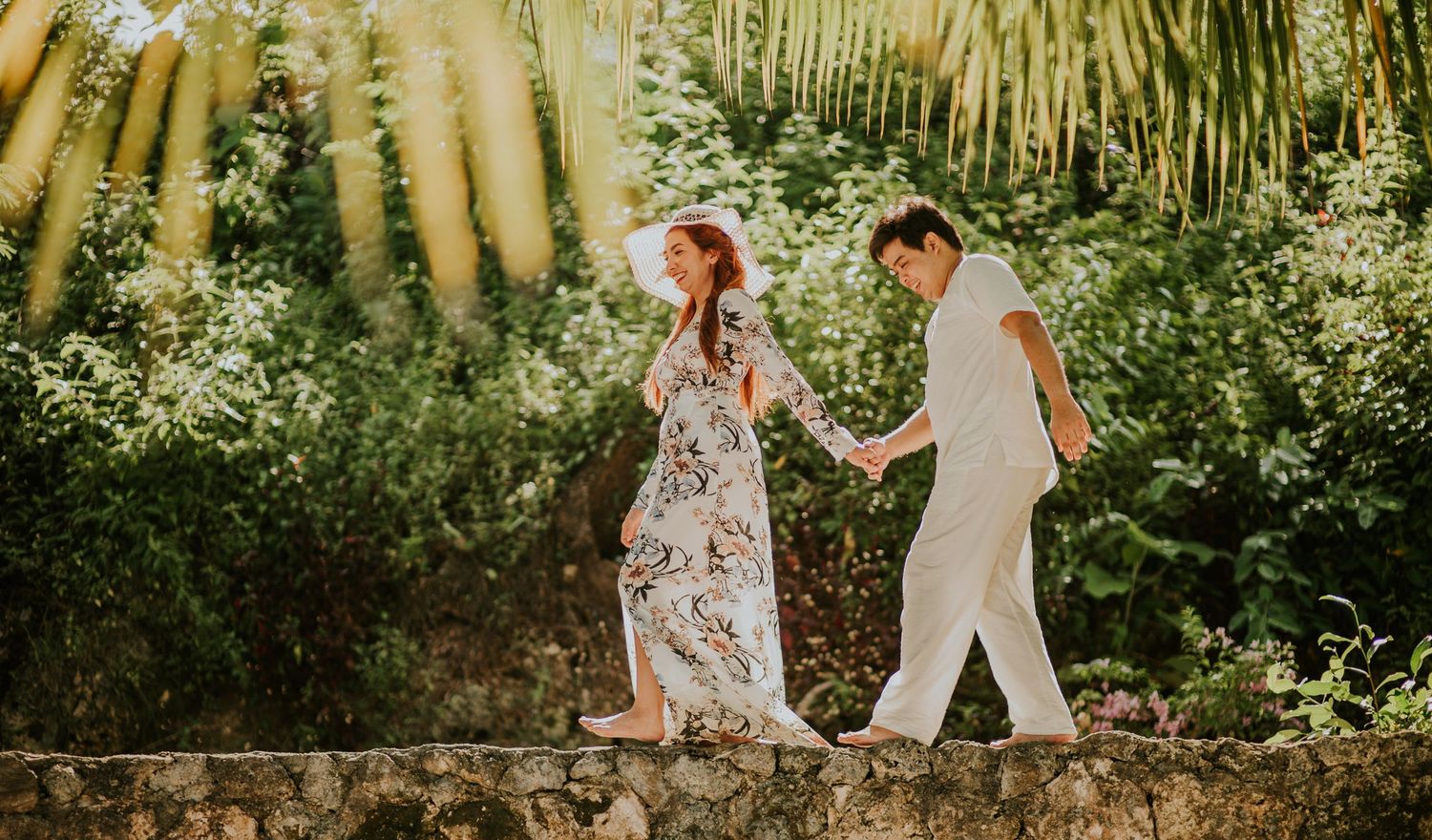A couple walking through lush tropical foliage and palm trees.