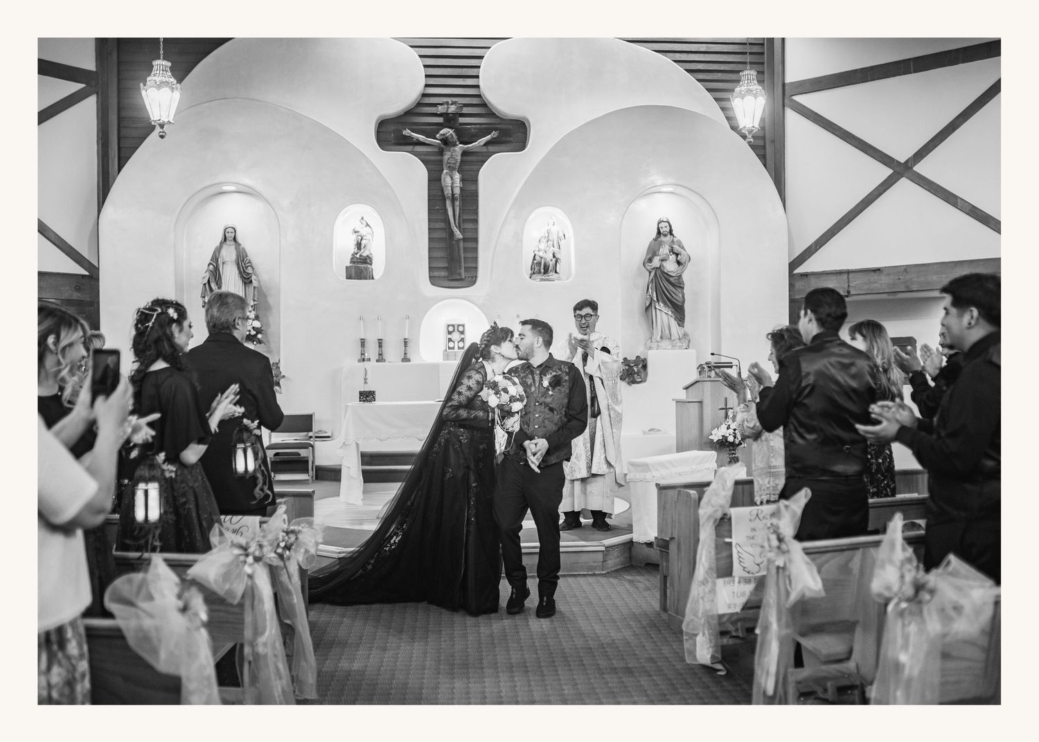 Black and white photo of a couple sharing a kiss at the altar during their wedding ceremony in a Catholic church.