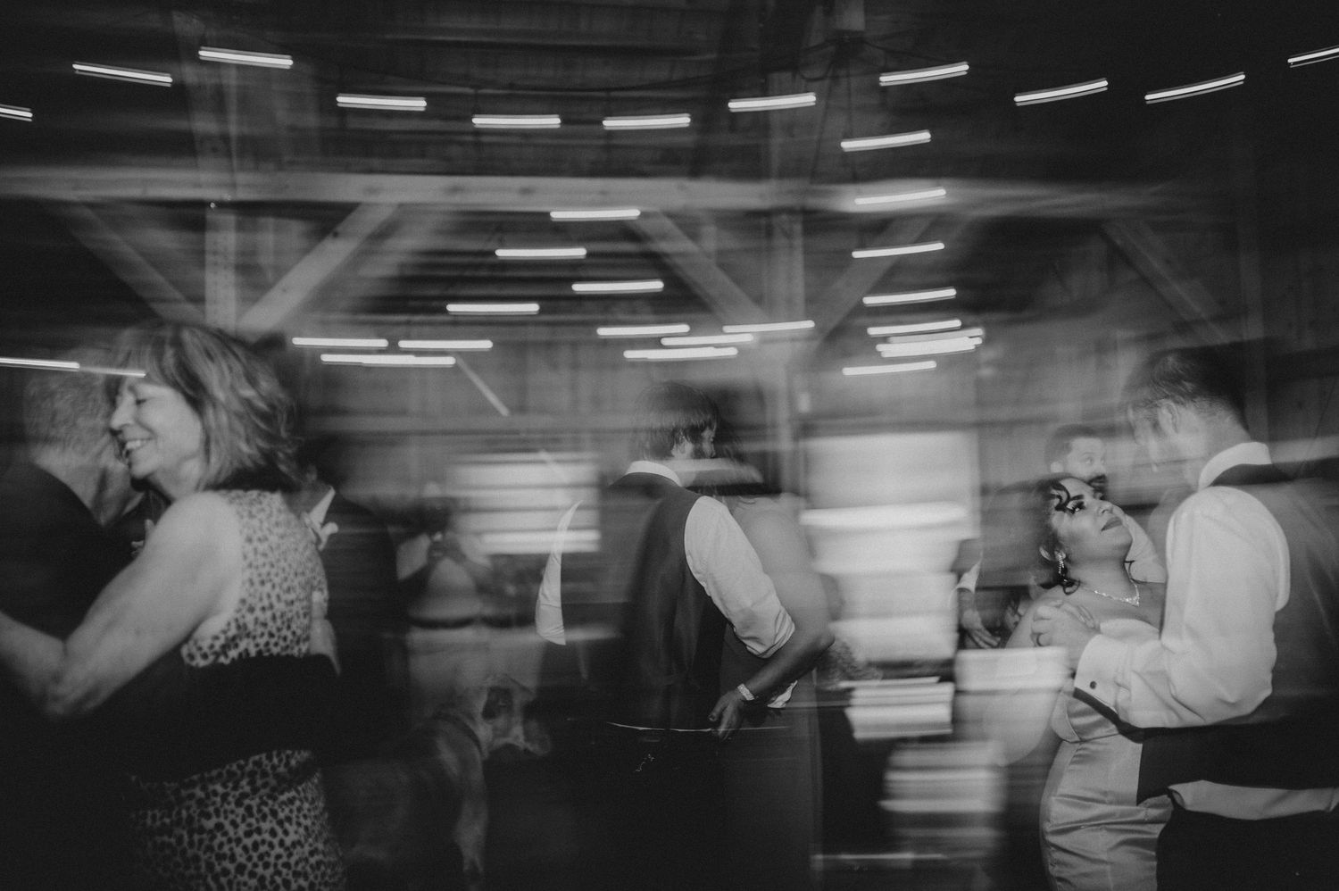 Black and white photo of dancers in motion on a dance floor with blurred movement and overhead lighting effects.