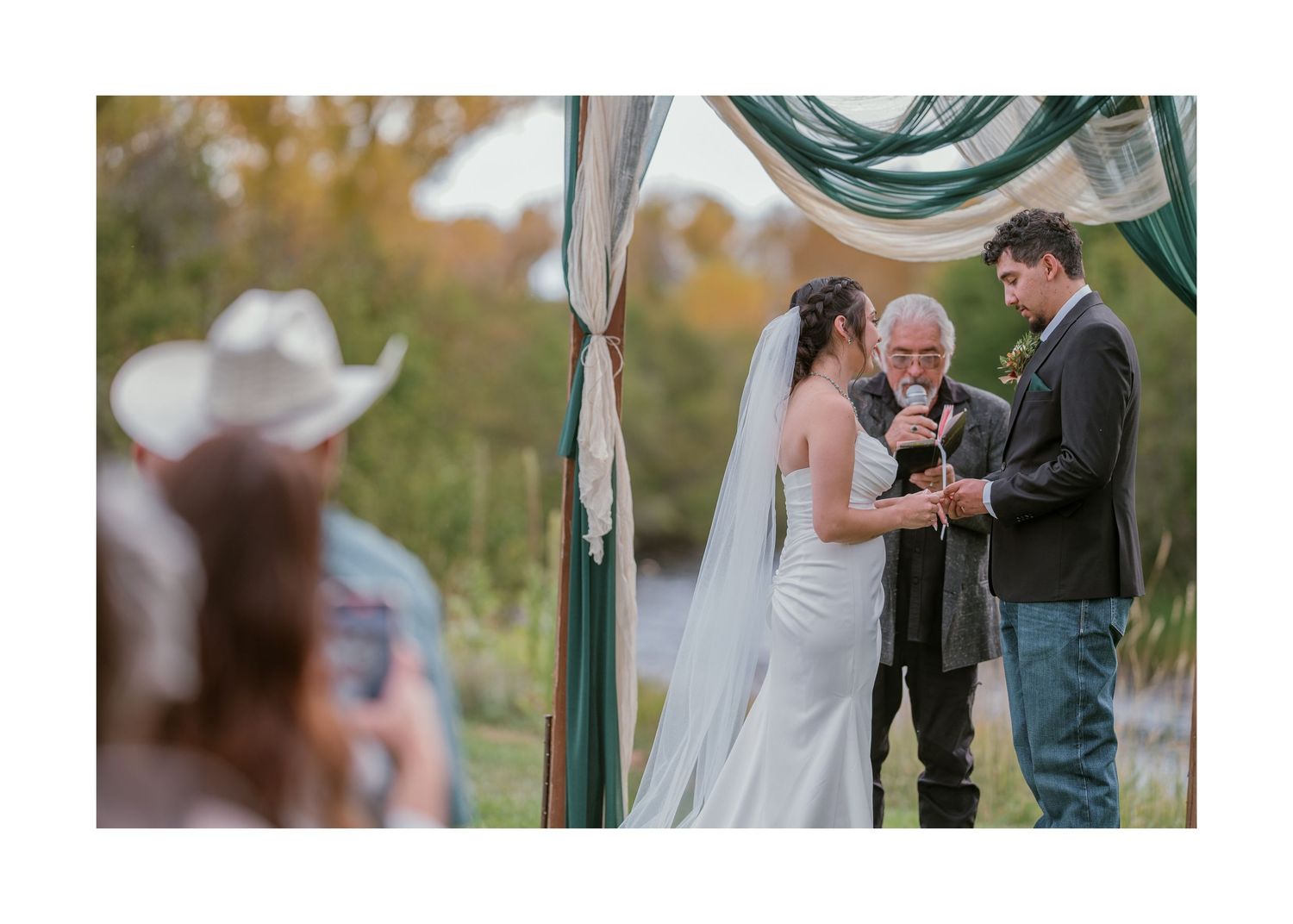 Intimate wedding ceremony taking place under a white fabric arch in an outdoor garden setting.