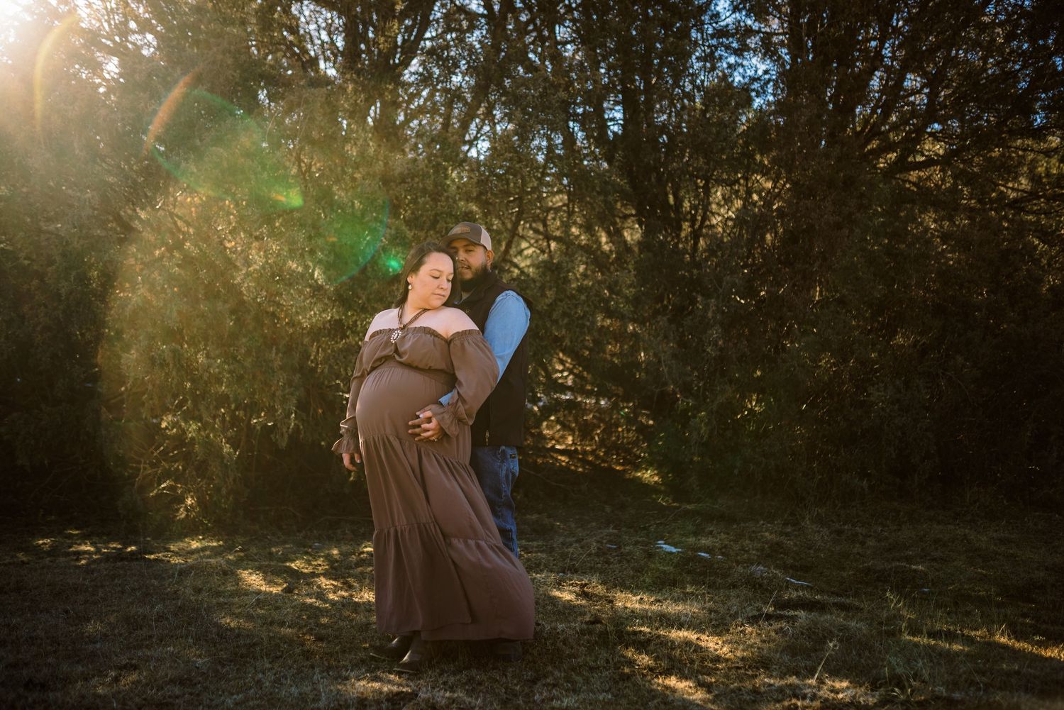 A couple embraces in a sun-dappled forest clearing during golden hour, creating a romantic outdoor moment.