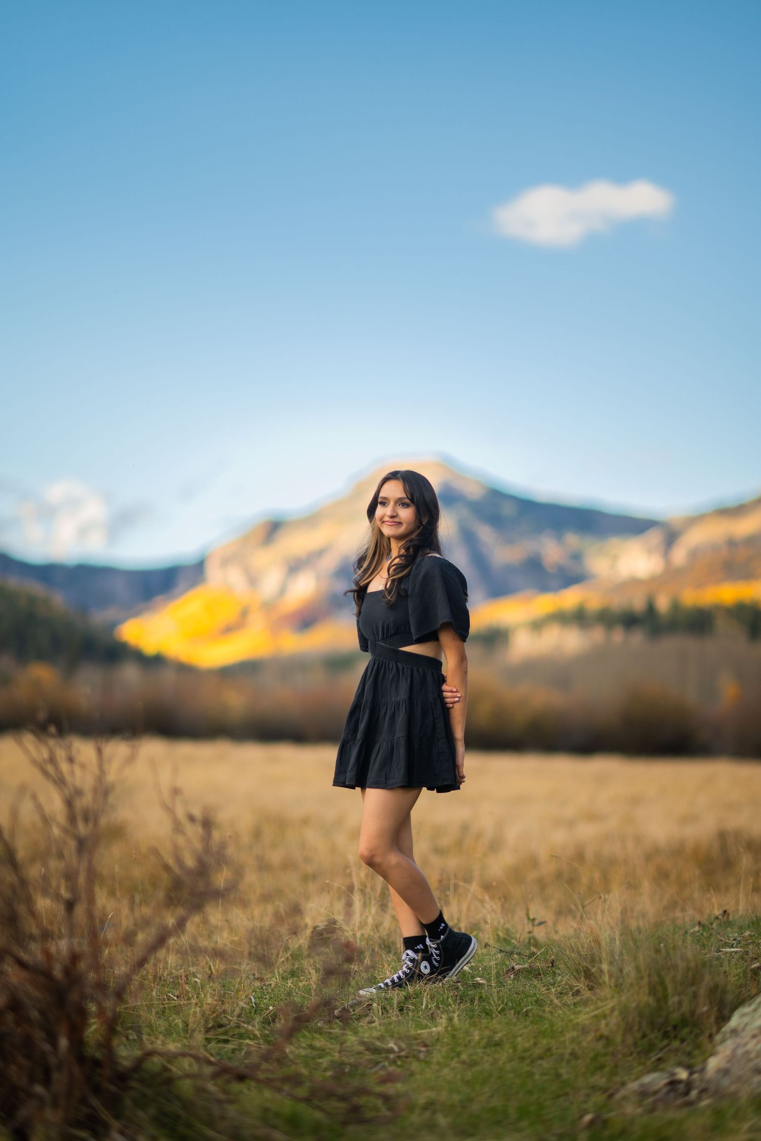 A figure in a black dress twirls gracefully in a scenic mountain meadow at sunset.