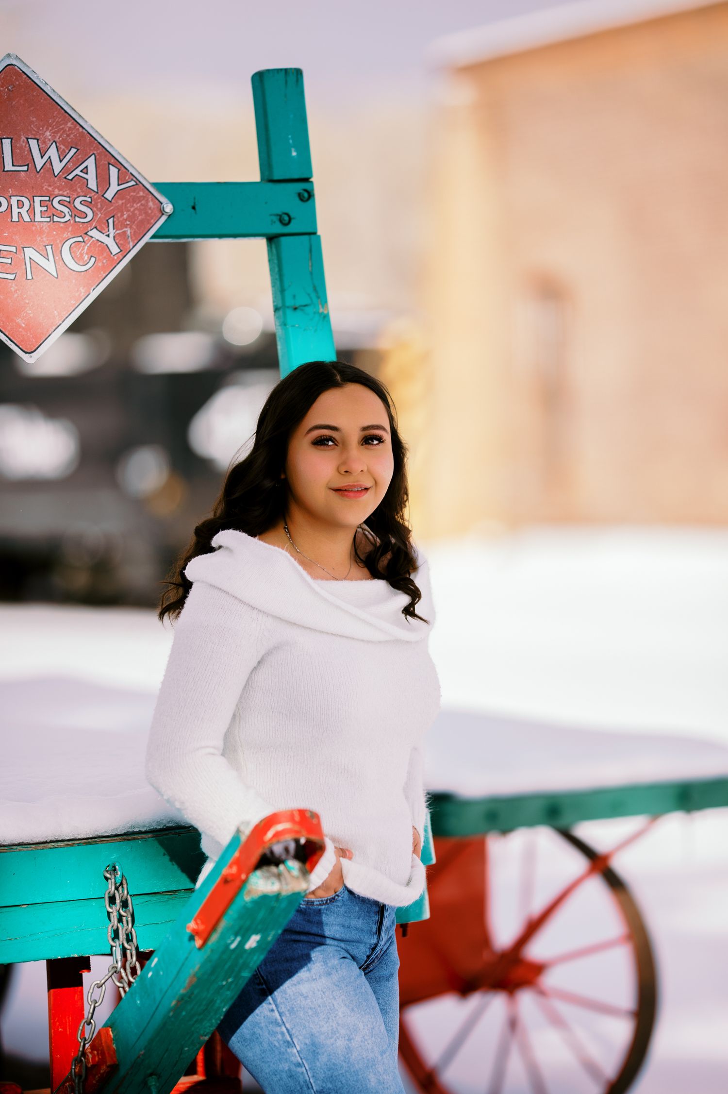 A woman in a white sweater and jeans poses outdoors against a turquoise railing in winter.