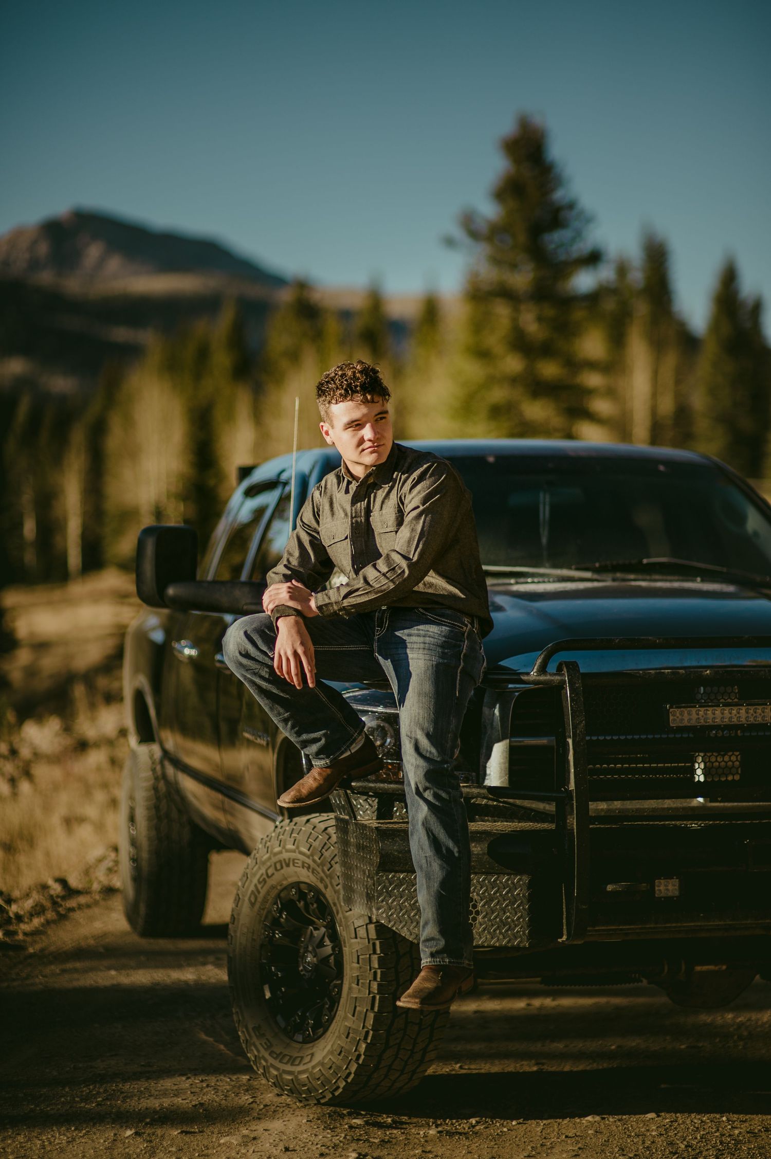 Casual portrait sitting on truck tire with mountain landscape in background.