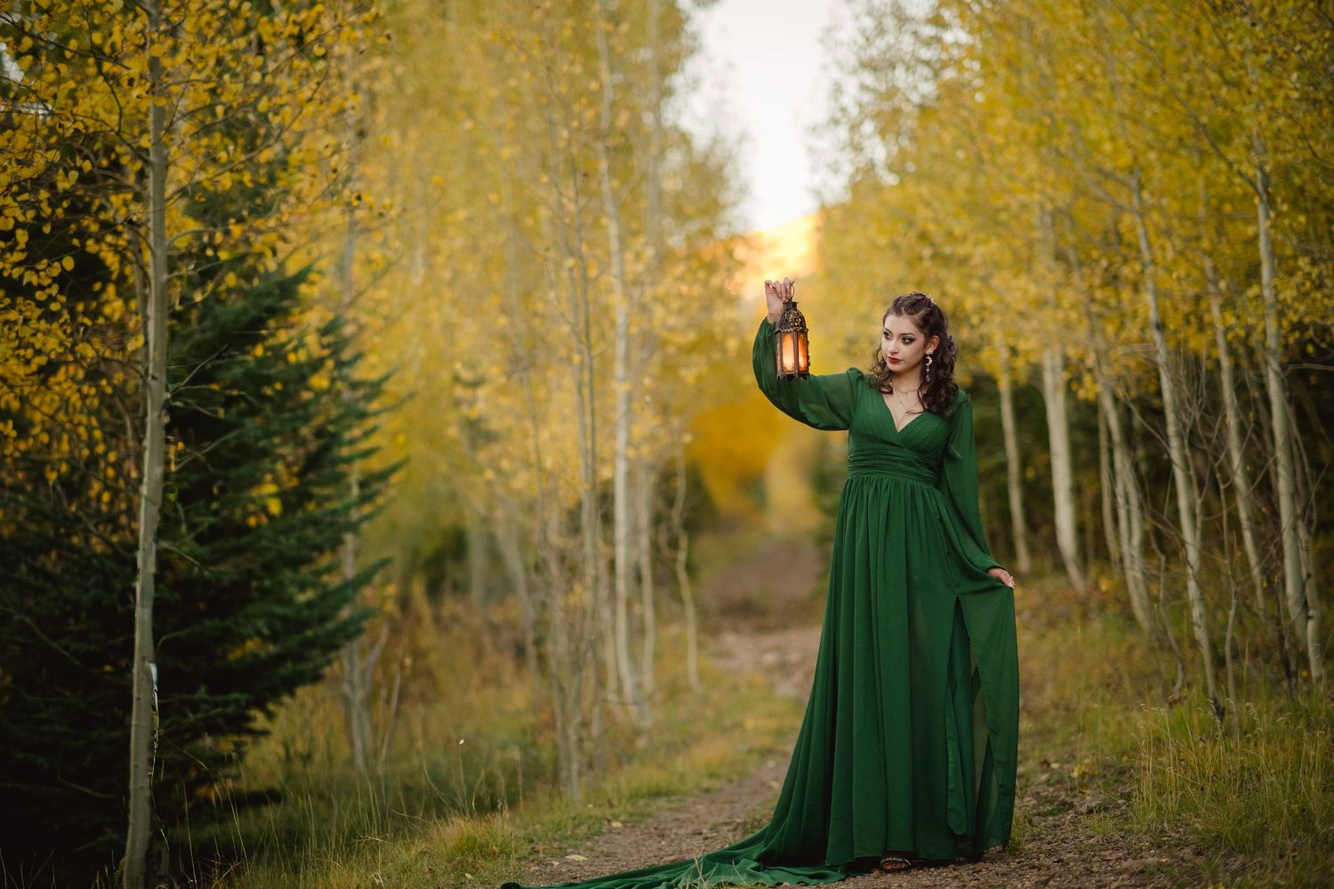 Ethereal forest scene with figure in emerald dress walking among golden aspen trees during fall.