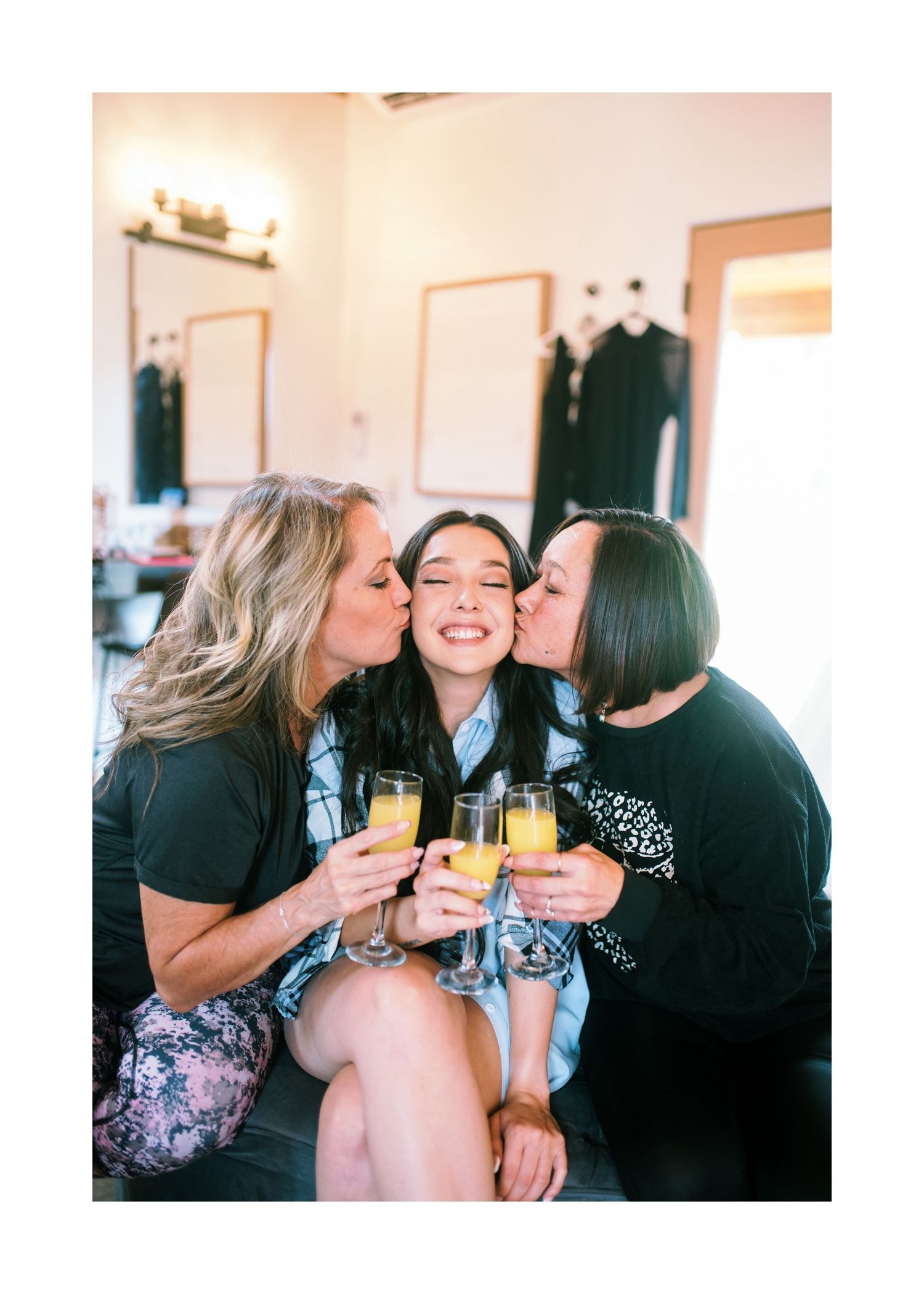 Three friends share drinks and joyful moments while toasting with mimosas at a casual indoor gathering.