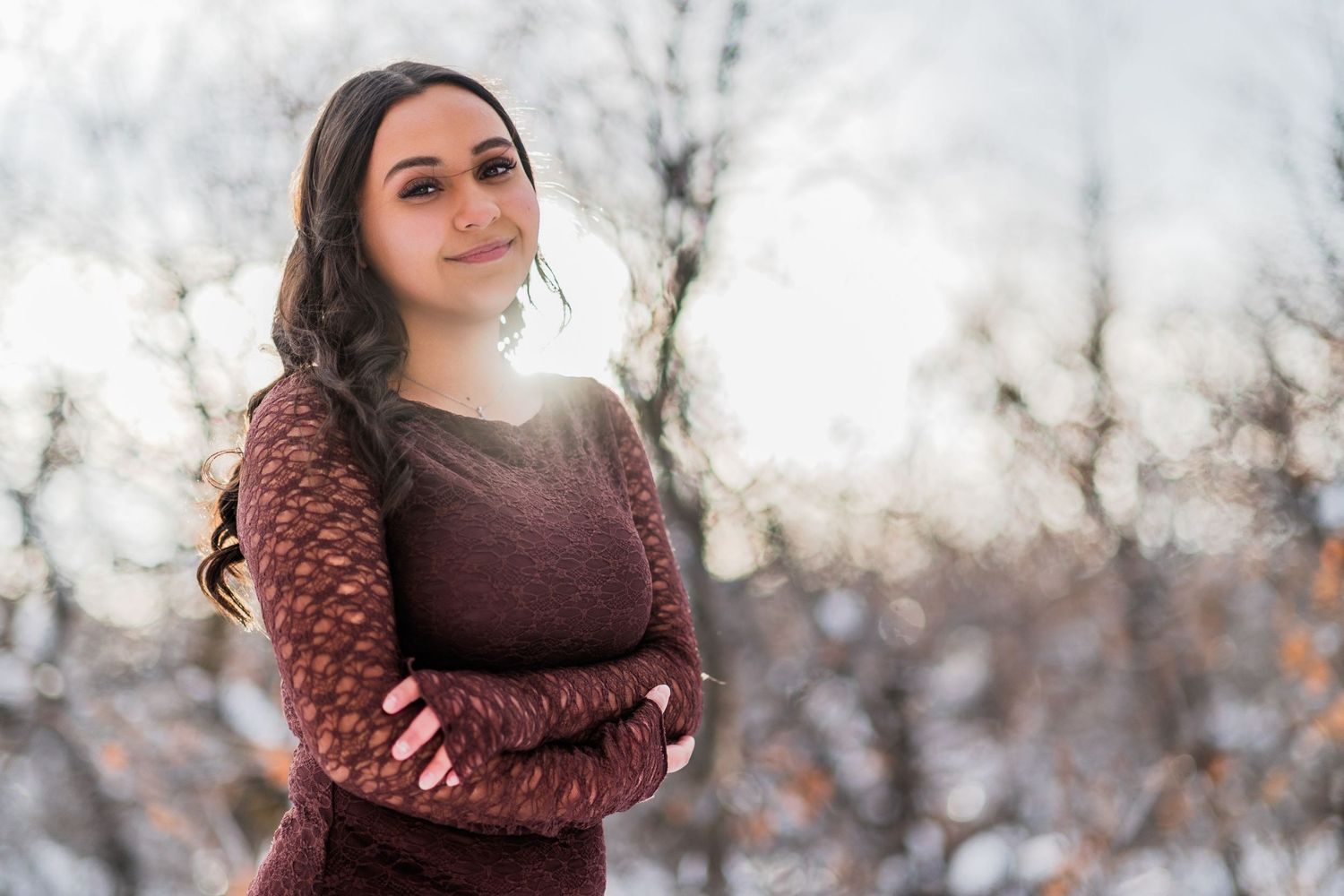 A person in a burgundy sweater poses outdoors on a bright winter day with snowy blurred background.