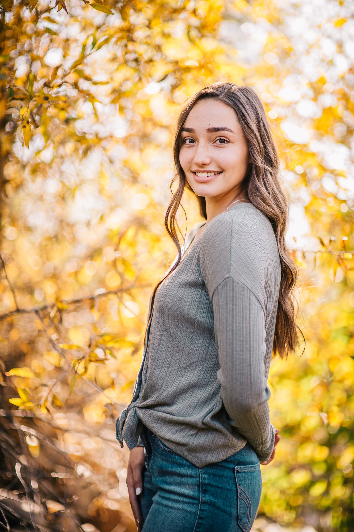 Fall portrait session featuring grey sweater and denim against golden autumn foliage.