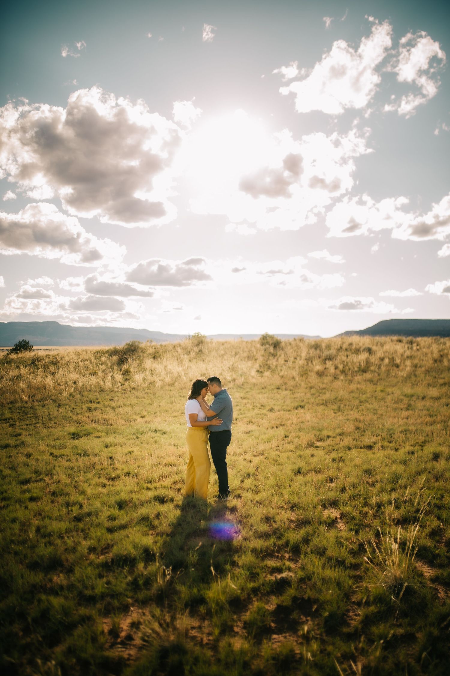 Couple embracing in a vast grassland under dramatic cloudy skies.