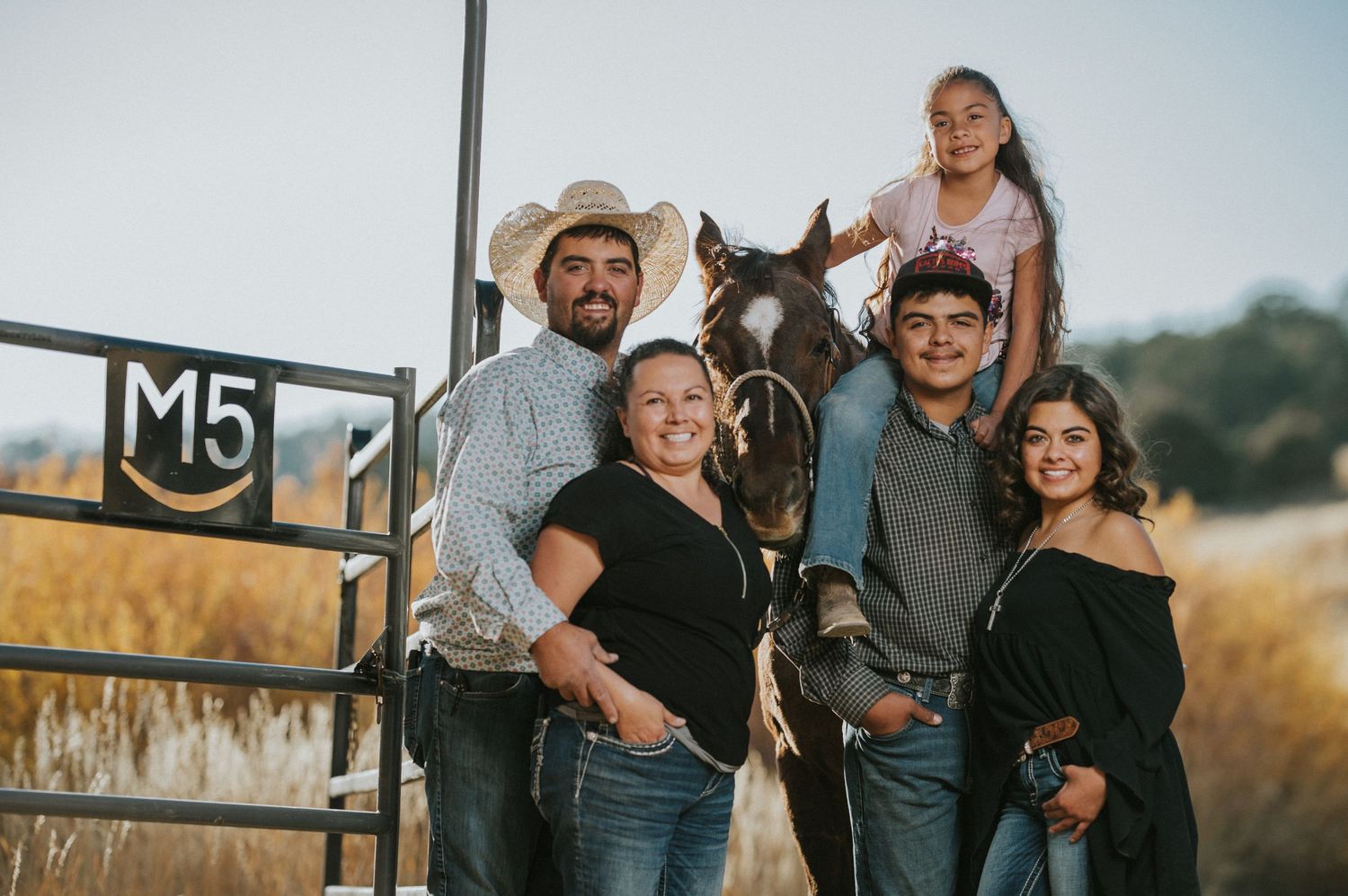 Group embracing in casual attire against rural backdrop with rustic fence.