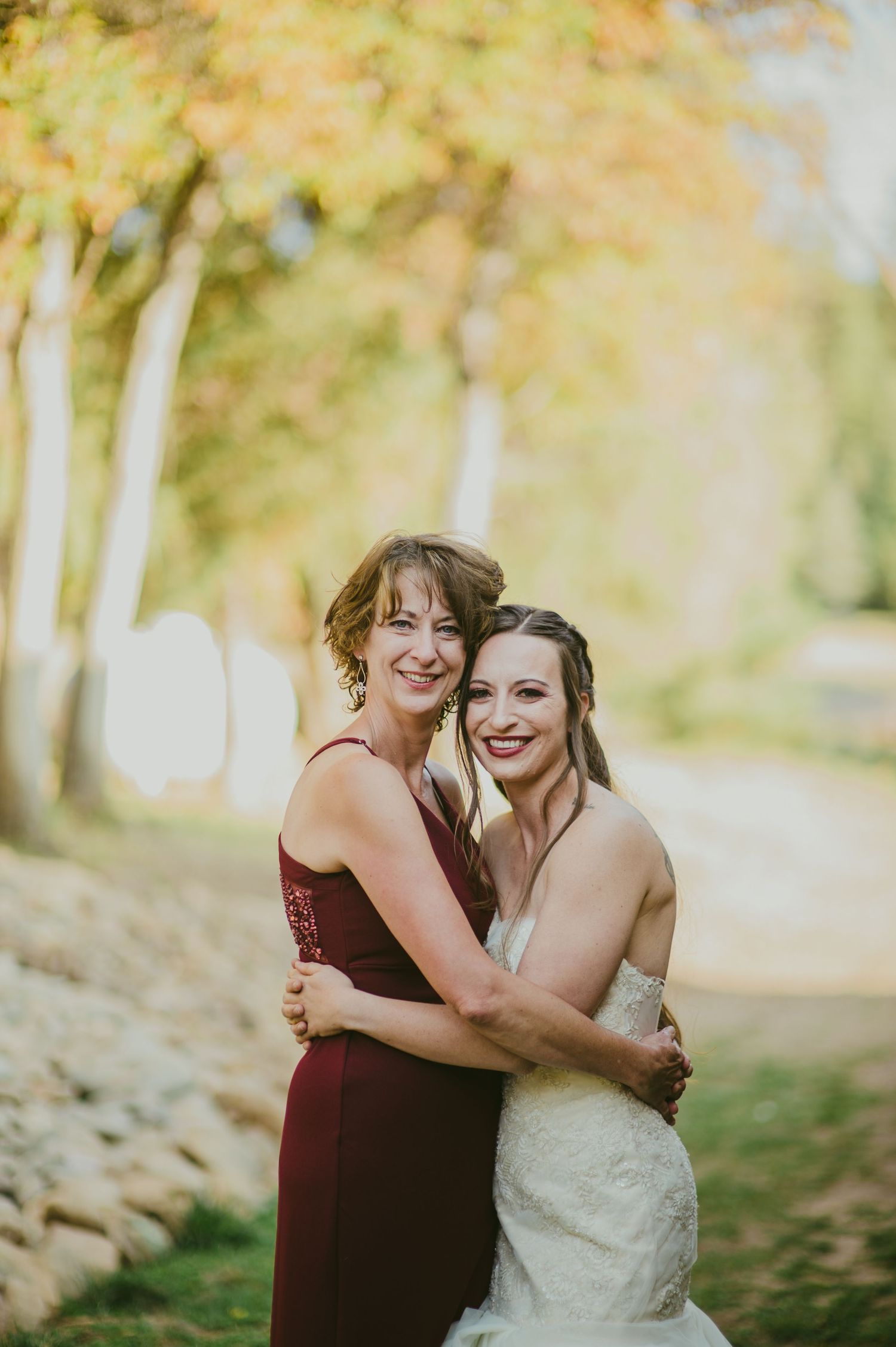 Intimate autumn wedding portrait with burgundy bridesmaid dress against yellow foliage.
