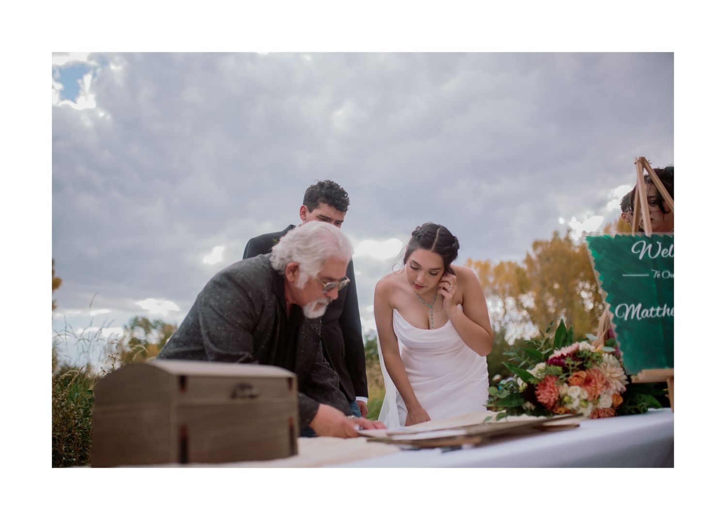 Newlyweds sign their marriage license at an elegant outdoor wedding ceremony table.
