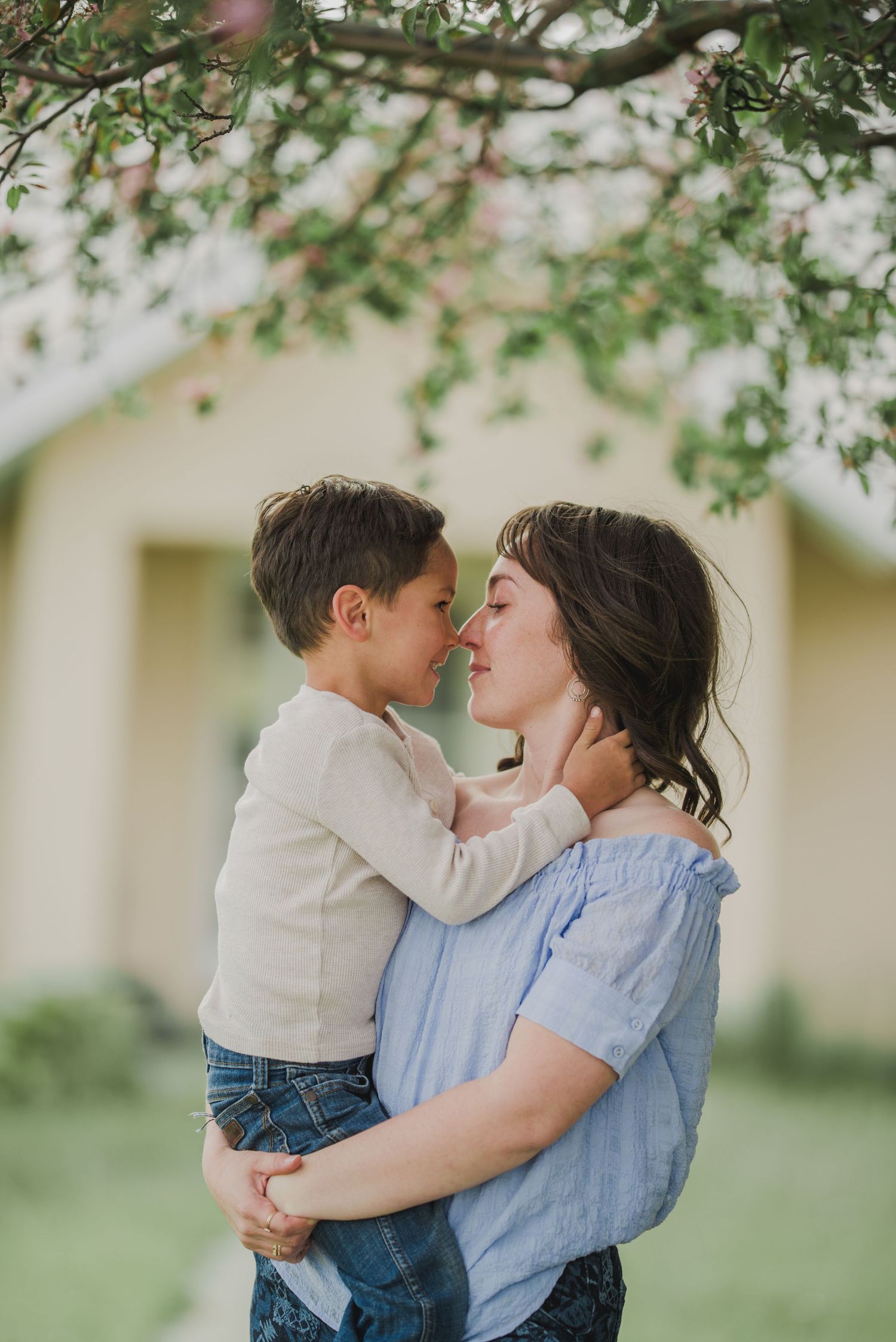 A tender moment between parent and child under blooming tree branches in springtime lighting.