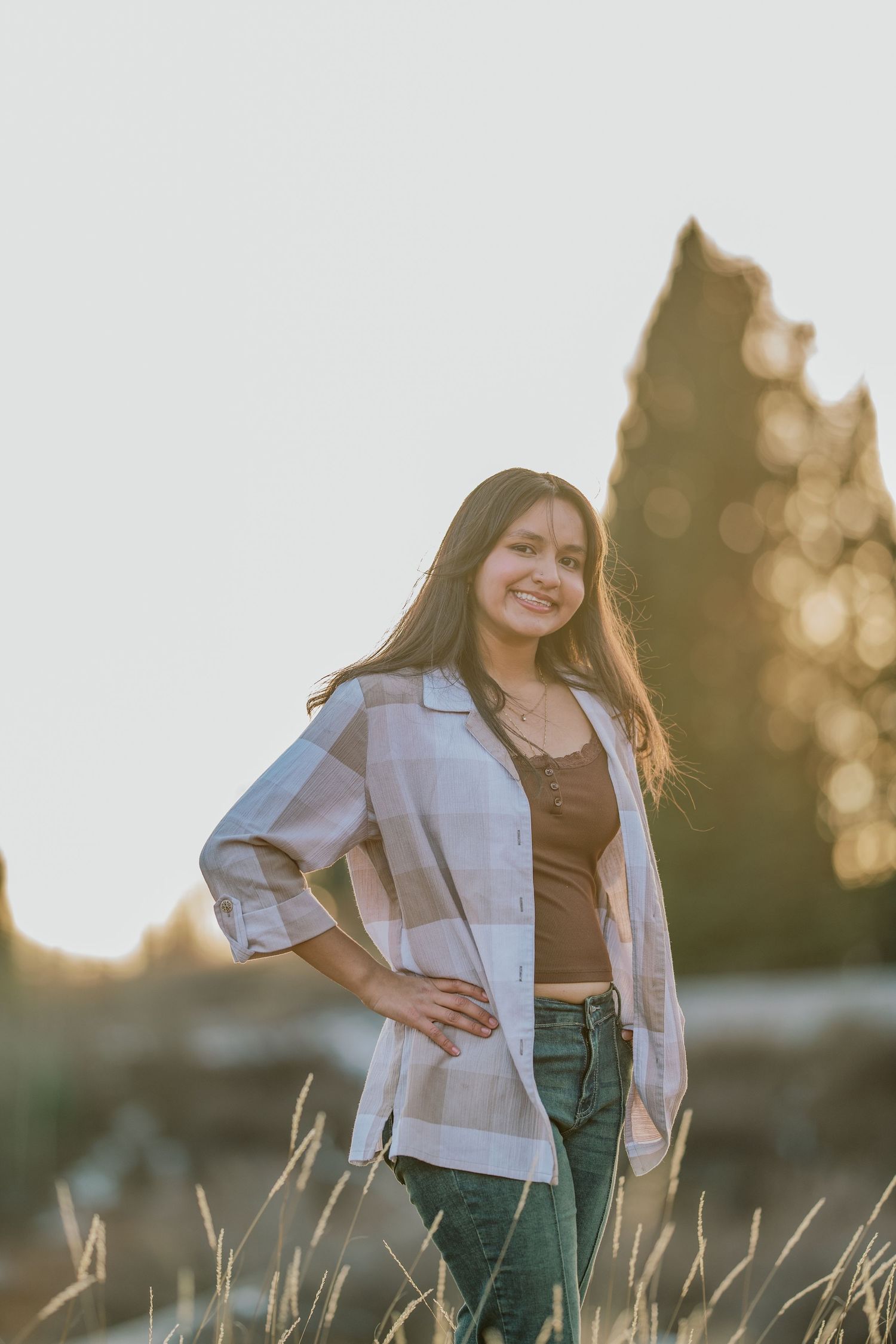 A person in a light jacket poses in a field of tall grass at golden hour with soft bokeh lighting effects in background.