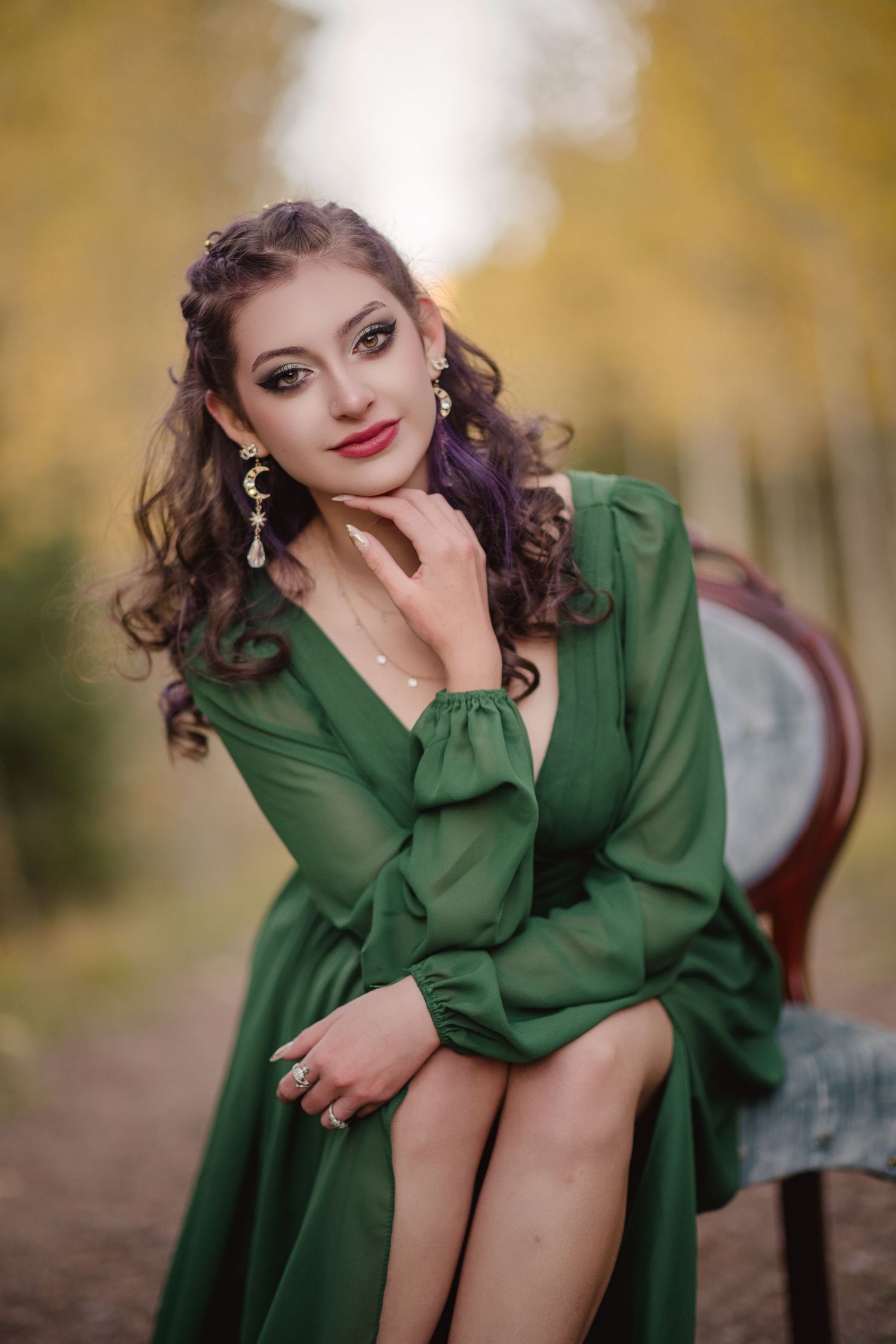 A person in a green coat poses outdoors against a blurred autumn background with golden bokeh lighting effects.