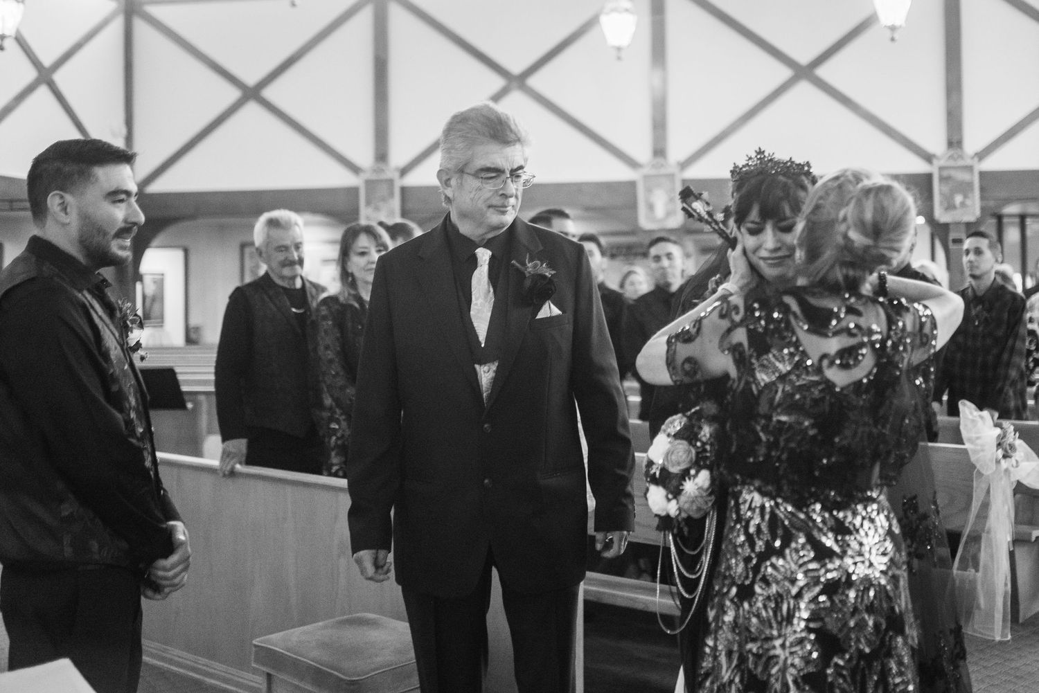 Black and white photo of elegantly dressed guests walking down church aisle during a formal wedding ceremony.