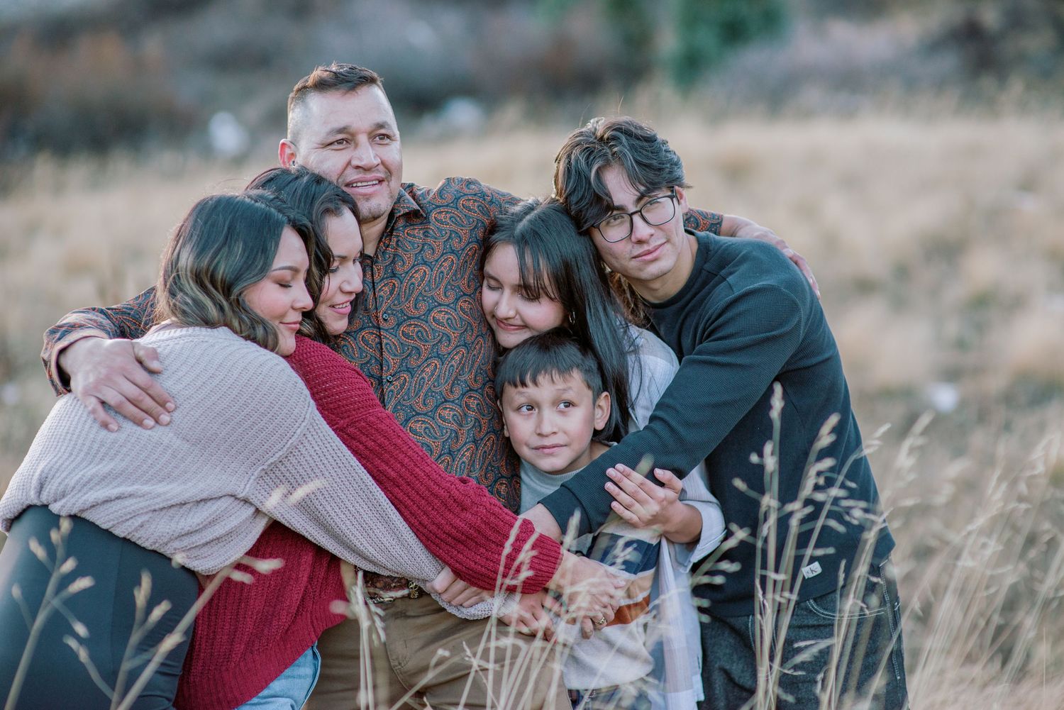 A series of candid outdoor family photos showing a group embracing and laughing together in a grassy field during autumn.