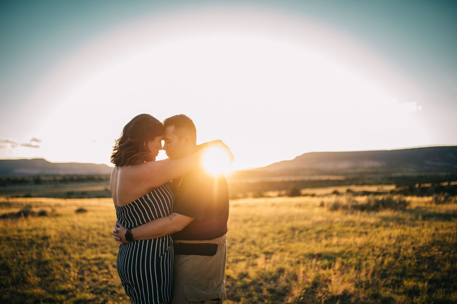 Silhouettes of a couple embracing against a warm sunset sky in an open field.